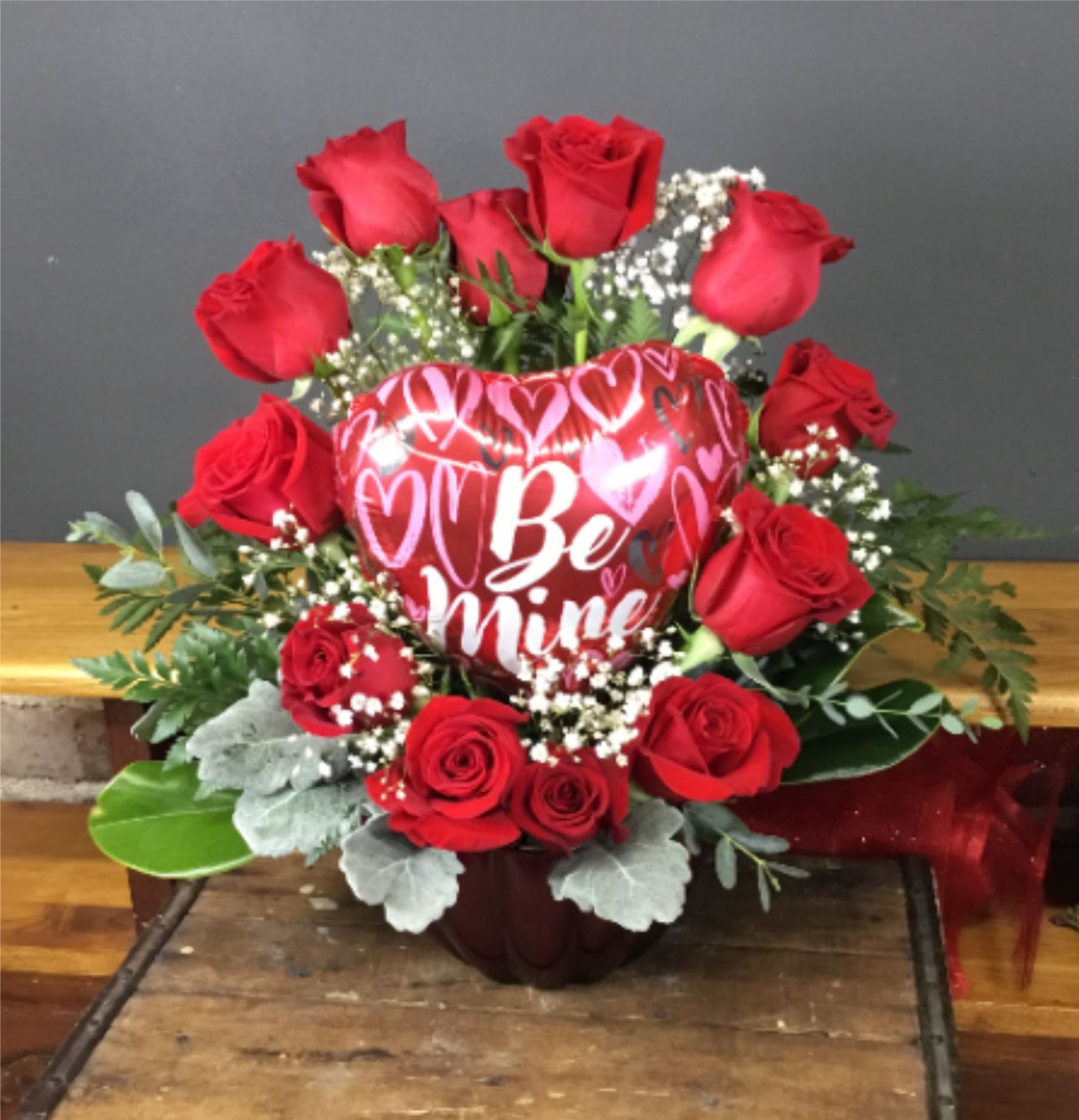 1 Dozen Heart Shaped Rose Arrangement - 1 Dozen Roses arranged in the shape of a heart in a reusable red bowl with a small Valentine Balloon with assorted Greens.