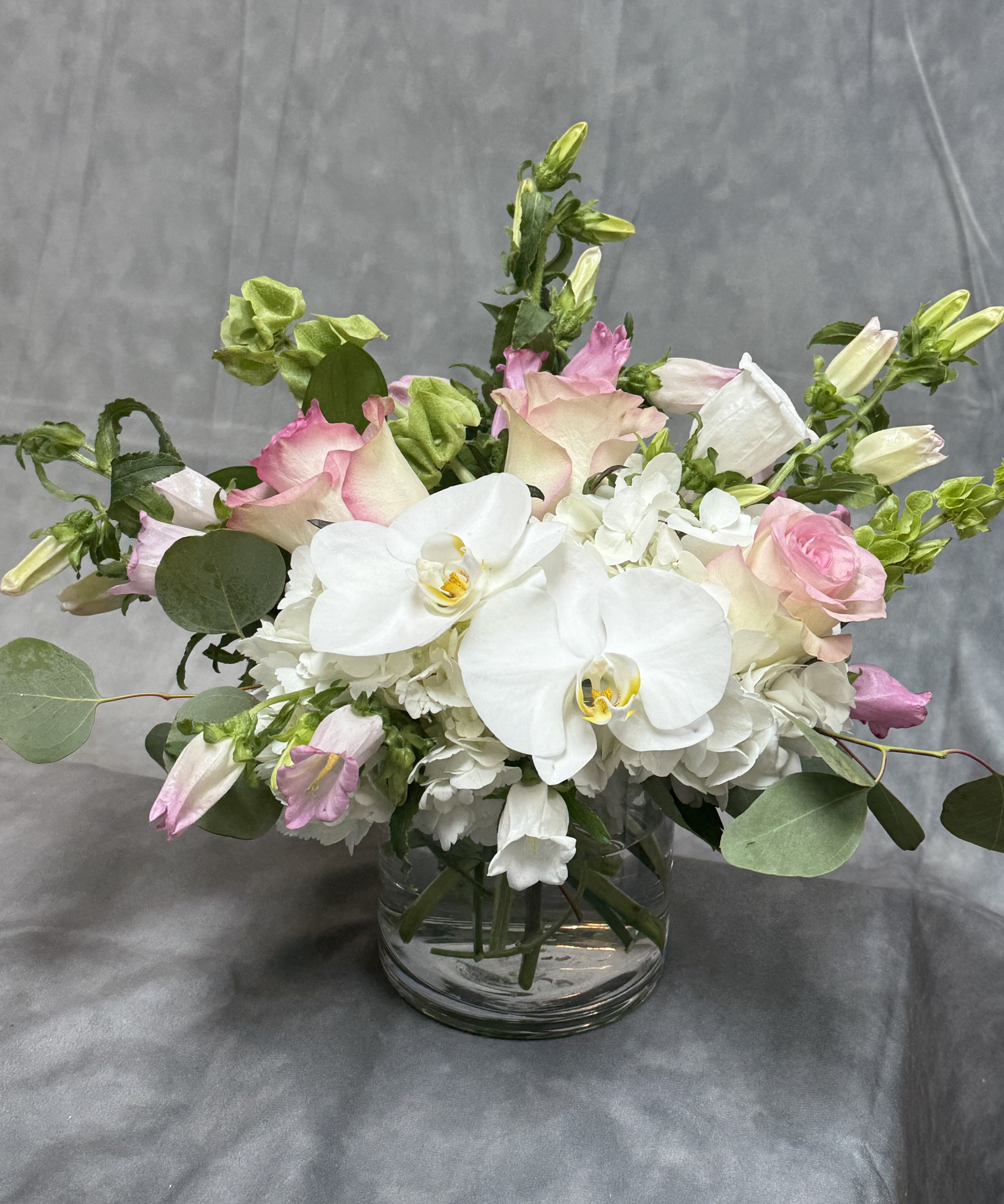Soft  Elegance  - Introducing Soft Elegance —a breathtaking new design that blends timeless beauty with a touch of sophistication. Featuring lush hydrangeas, delicate orchids, fragrant stock, vibrant roses, graceful delphinium, and charming ranunculus, all arranged in a sleek low vase. Perfect for adding effortless elegance to any space or occasion. 