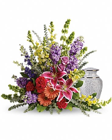  Shades Of Faith - A rainbow of reverence. This uplifting arrangement of lilies, roses and snapdragons is a beautiful reflection of a colorful life well lived. Pink stargazer lilies, lavender roses and yellow snapdragons are arranged with peach gerberas, hot pink carnations, lavender stock, bells of Ireland, purple larkspur, spiral eucalyptus and lemon leaf. Arrangement does not include urn. Approximately 29" W x 25 1/2" H