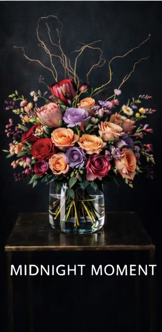 Midnight Moment Arrangement - A dramatic, high-impact statement designed to stop time. Our most elevated Valentine’s arrangement, Midnight Moment showcases premium garden roses—Queen of Hearts, Queen’s Crown, and Phoenix—selected at peak openness for richness, depth, and intensity. Sculptural protea adds bold structure and an editorial edge, while elegant branches create a cinematic silhouette and a sense of motion above the blooms. Luxe, confident, and unforgettable—made for grand gestures and after-dark romance.