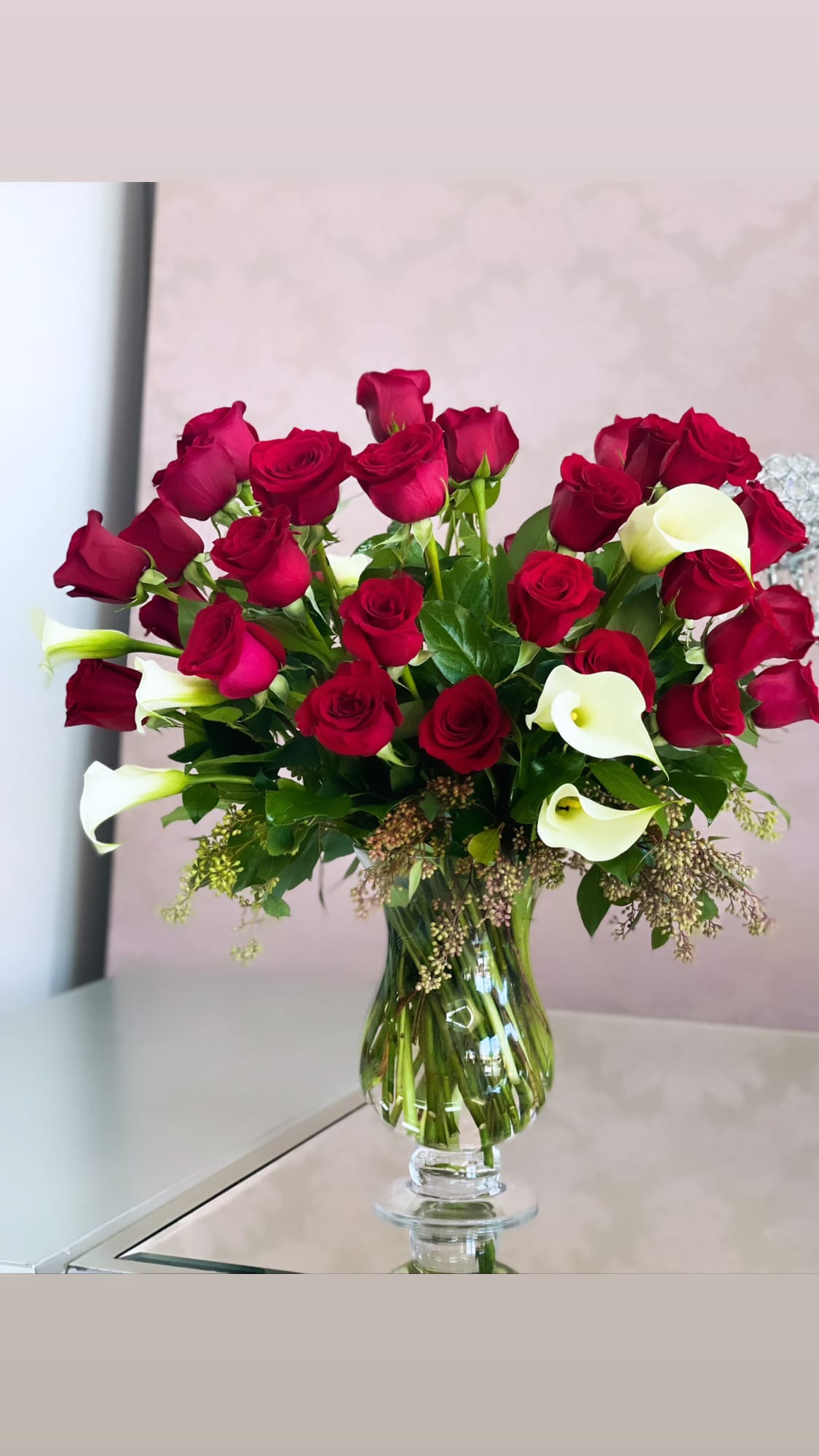 Be Still My Heart - 24 red roses &amp; white mini callas  - The look of love is charmingly reflected in this romantic array of red roses and fragrant white callas. Beautifully presented in a sparkling glass vase, these gorgeous flowers will say what's in your heart more eloquently than words.  The gorgeous bouquet features one dozen red roses and a half dozen miniature white calla lilies accented with assorted greenery.  Approximately 15 1/2" W x 15 1/2" H  Orientation: All-Around     