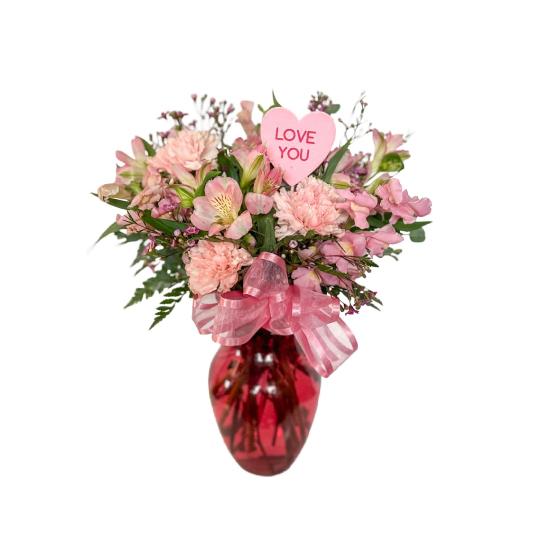 PINK - PINK is a soft and romantic arrangement featuring blush pink carnations, delicate alstroemeria, and seasonal accent blooms, designed with fresh greenery in a rich red glass vase. Finished with a pink ribbon and a sweet “Love You” heart pick, this arrangement is a heartfelt way to express love, appreciation, or affection for any occasion.