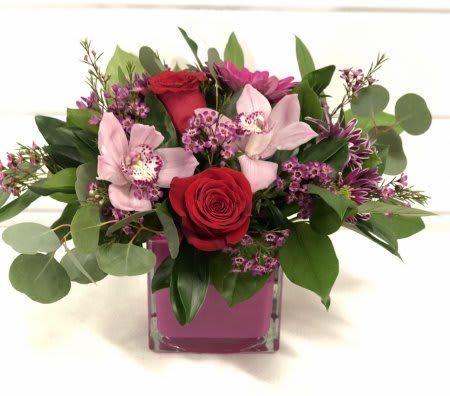 Orchids &amp; Roses - Stunning red roses combined with lush cymbidium orchids and arranged with mixed greenery into a glass vase.  