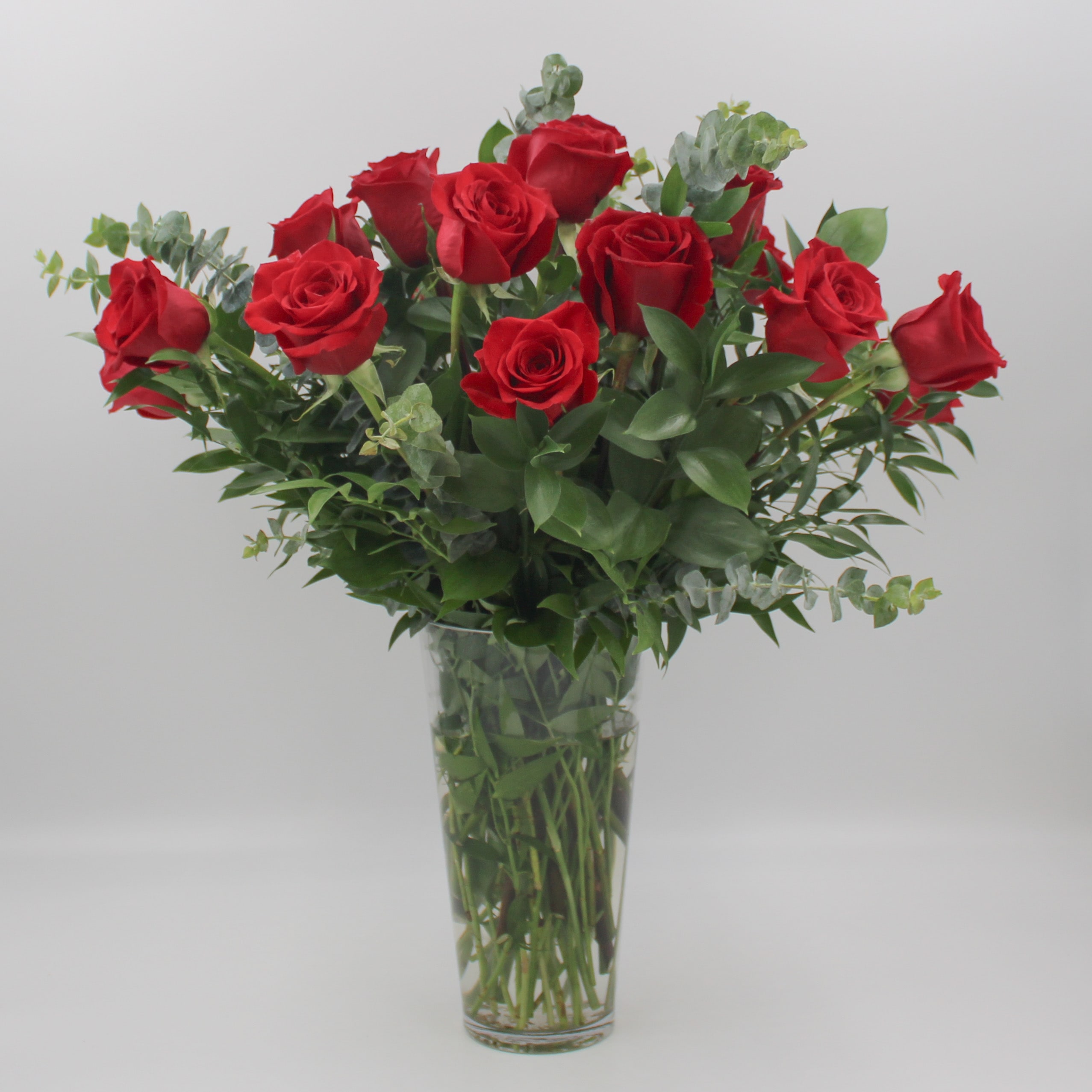 Two Dozen Red - A Classic dozen Ecuadorian Long Stem Red Roses  includes upscale greens such as Ruscus and Eucalyptus in a clear glass Riviera vase.