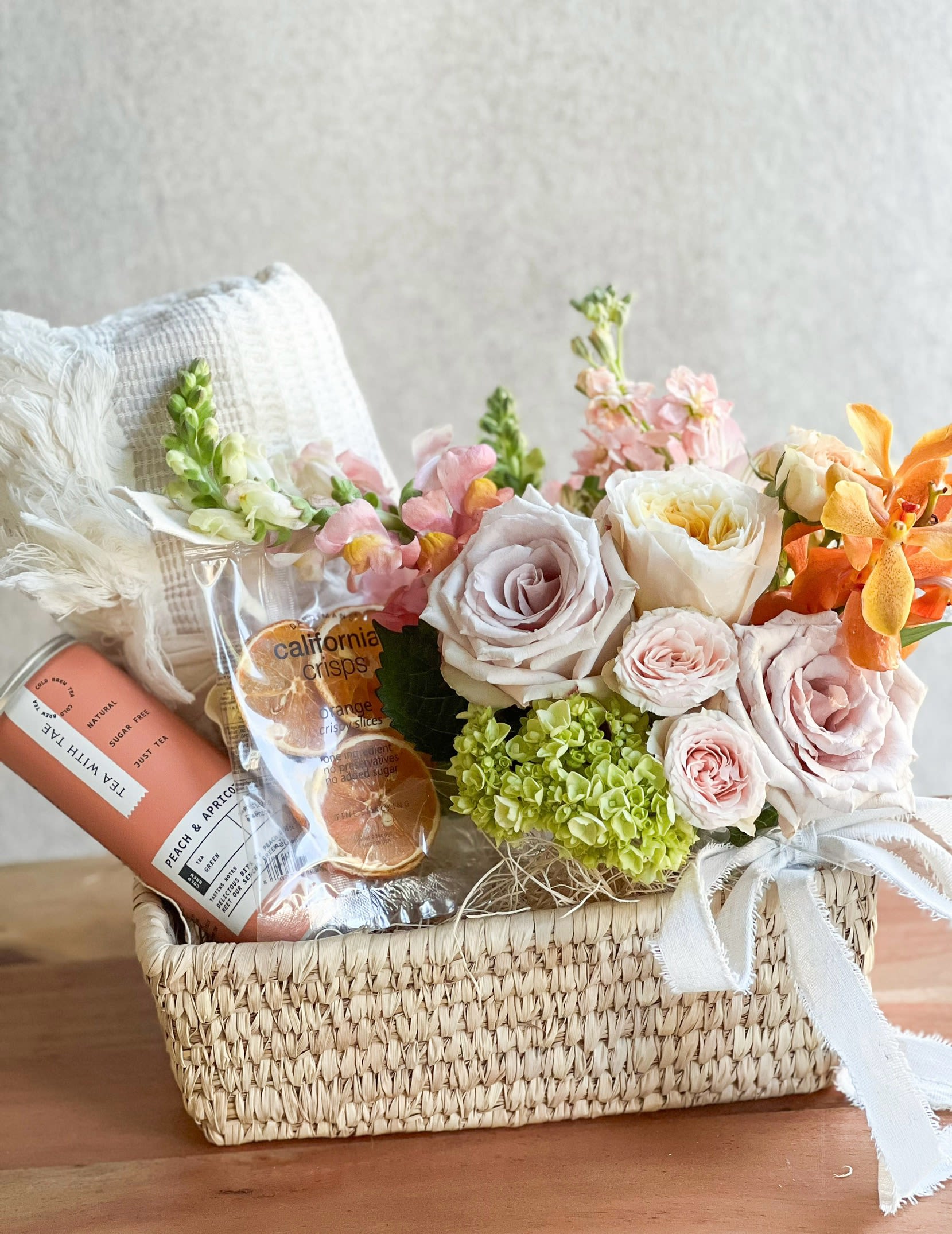 Blissful Harmony  - Give the gift of relaxation. This basket is perfect for a thoughtful gift. It includes a handwritten card and a combination of soft pastel flowers, peach and apricot tea, dried citrus crisps, and a cozy blanket in a basket. 