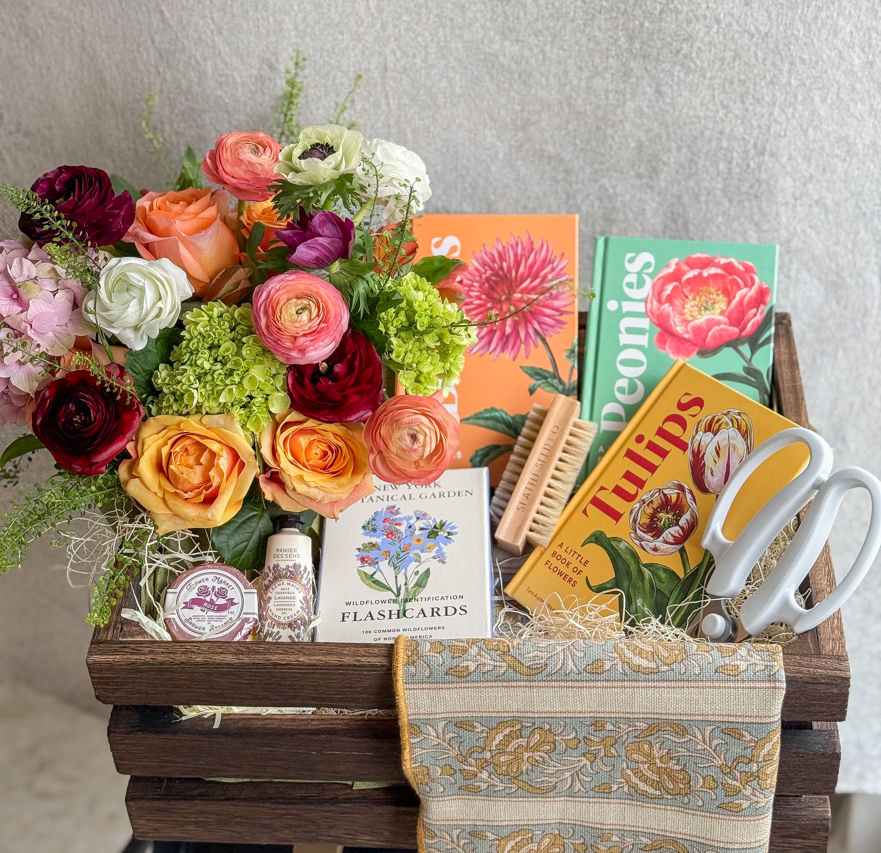 Flower Enthusiast Gift Basket - Gift in good taste with this elegant assortment of gifts any flower enthusiast will love!  A seasonal lush floral arrangement, a pair of shears, floral tea towel, wildflower identification cards, lavender hand cream, rose shower steamer, nail and veggie brush, and three floral books all about: (Peonies, Tulips and Dahlias)  All designed in a large wooden crate, includes handwritten card.   You deserve the best. If an item is unavailable, we’ll sub in products of equal or greater value.