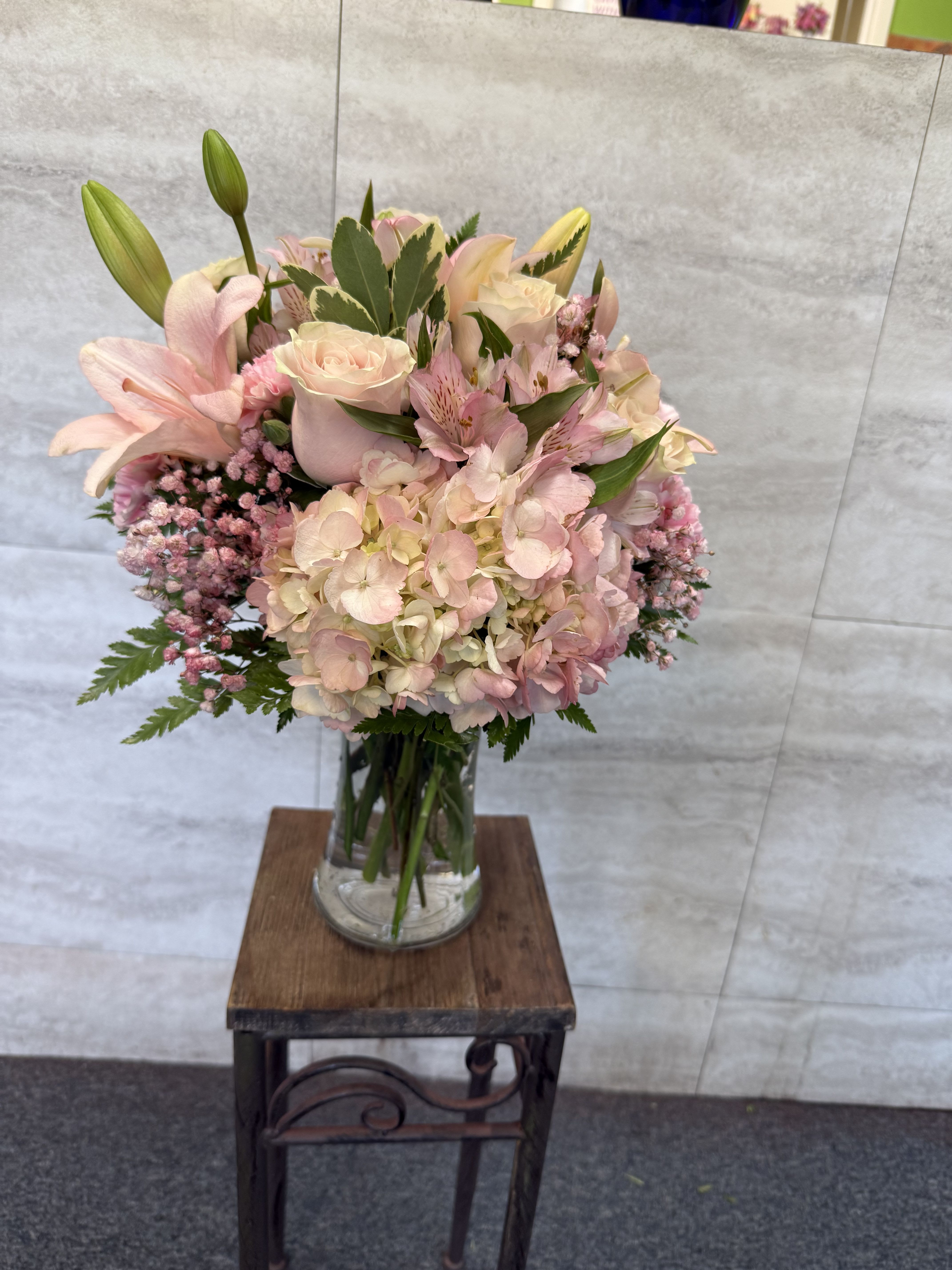 Country picnic bouquet  - A soft, pastel floral arrangement featuring blush hydrangeas, pale pink roses, pink lilies, alstroemeria, and delicate pink statice, accented with fresh green foliage in a clear glass vase. 