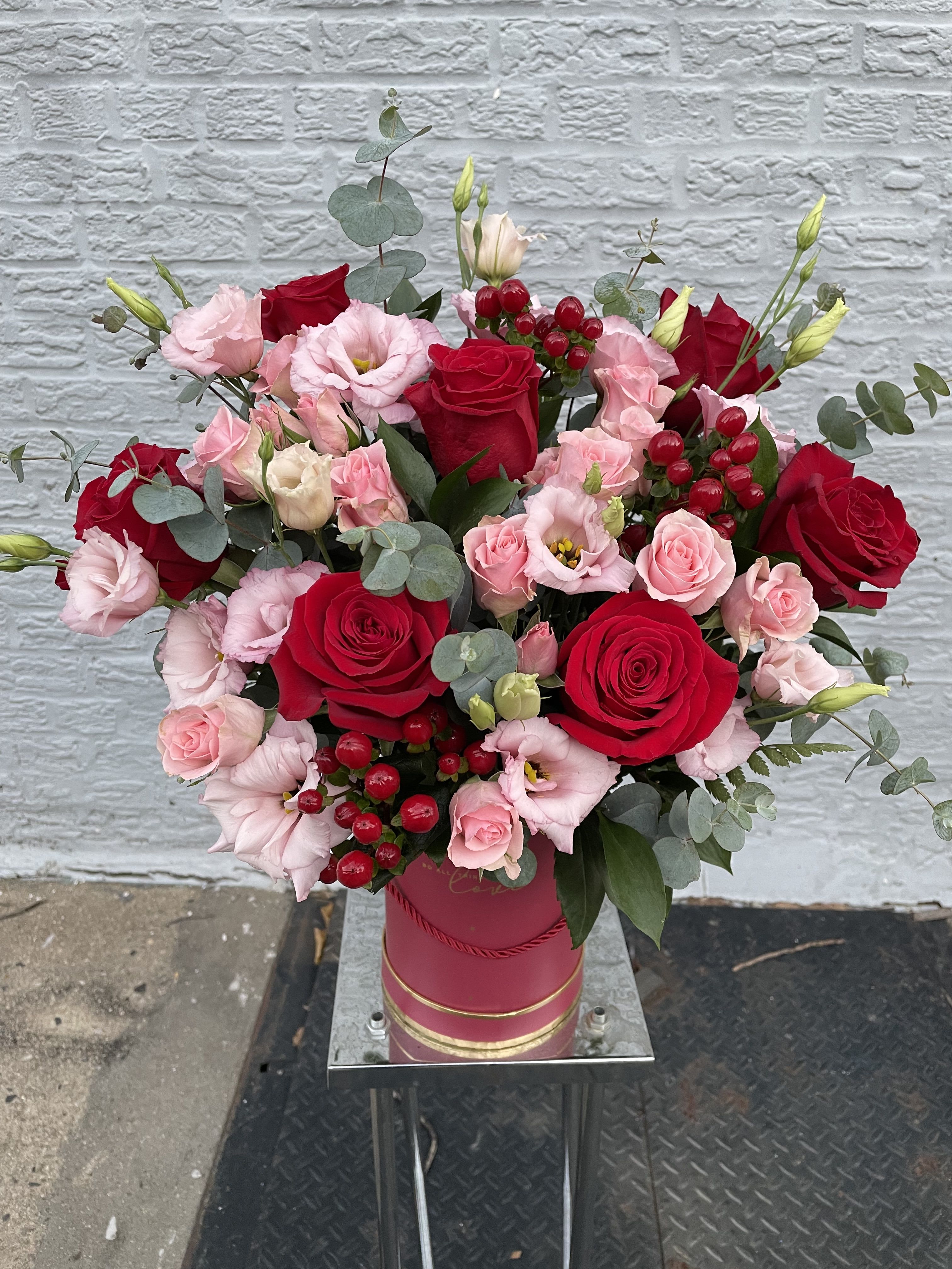 Flower arrangement “Charm” The Photo Shows A Deluxe Size. - Created with red roses, complemented by delicate lisianthus and spray roses, beautifully paired with fragrant eucalyptus.