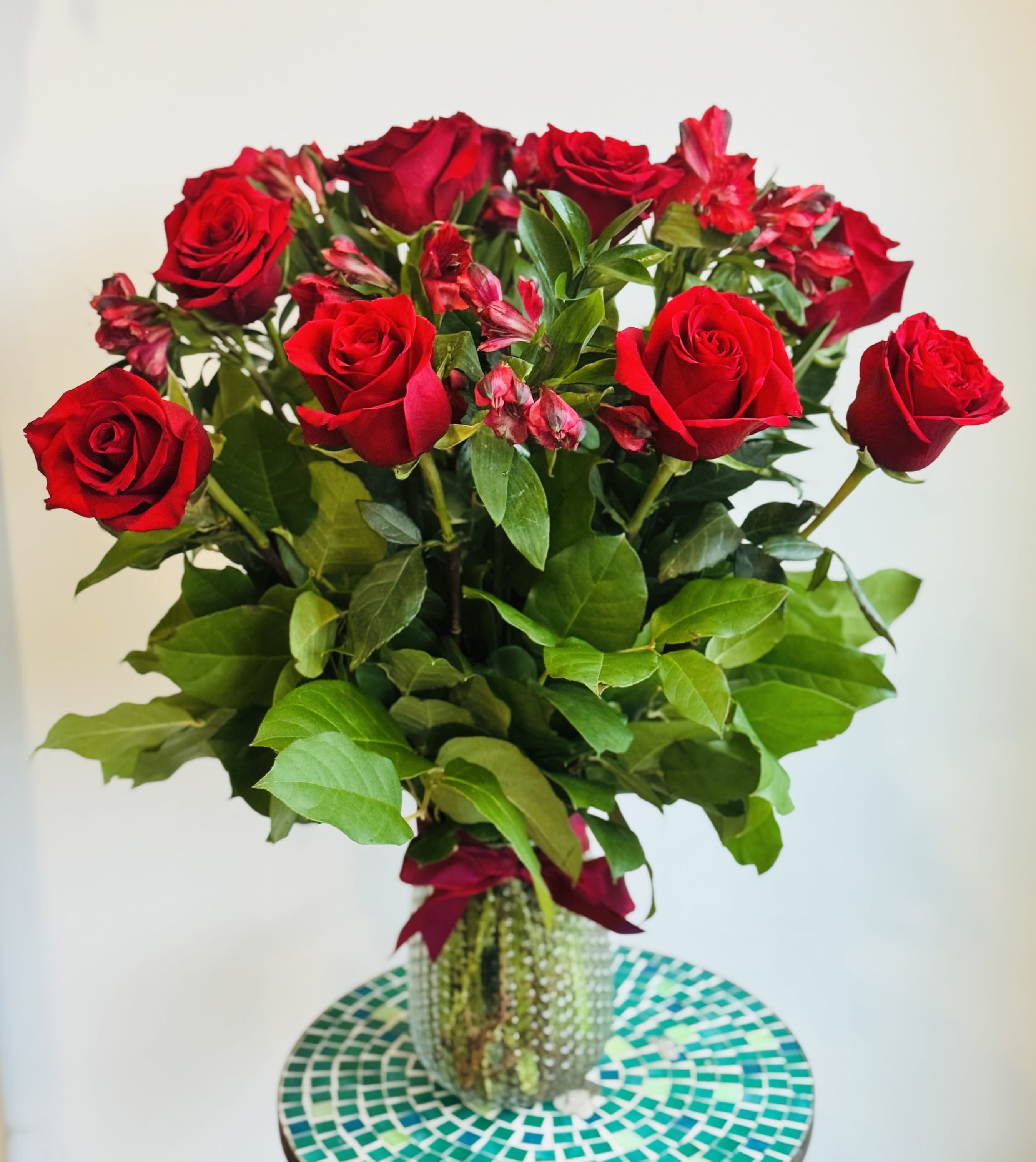 Dozen Roses (red may or may not be available) - A dozen roses arranged with greenery and seasonal fill flowers in a clear glass vase. Please specify if you want low and lush or tall and grand