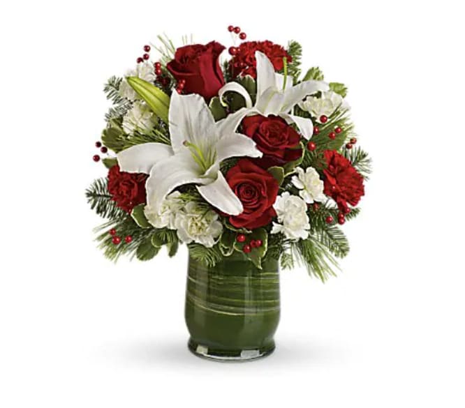 Holiday Hues Bouquet - Bright as the northern star, majestic white lilies shine against a lush backdrop of rich red roses, fresh seasonal greens and festive berries. It's the perfect way to show you love them this holiday season. This chic holiday arrangement features white oriental lilies, red roses, miniature white carnations, red carnations and jolly red berries. Seasonal greens include white pine, douglas fir, and noble fir. The flowers are delivered in a beautiful glass hurricane vase lined with a green ti leaf.   Orientation : One-Sided  All prices in USD ($)  Standard  T597-2A  
