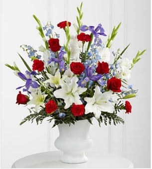 Cherished Farewell Arrangement - The Cherished Farewell Arrangement is an elegant display of patriotic beauty to honor your loved one at their final farewell service. Red roses, red carnations, white gladiolus, light blue delphinium, blue iris, white Oriental lilies, white Asiatic lilies and lush greens are elegantly arranged in a white plastic urn to create a stunning way to say your last goodbye. The standard arrangement is approximately 32"H x 26"W