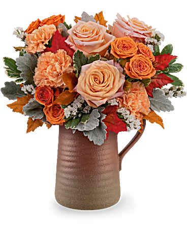 Cider &amp; Clay Bouquet - The Cider &amp; Clay Bouquet brings cozy autumn charm to any space. Featuring peach roses and orange blooms in a rustic stoneware pitcher, it's a beautiful gift for Thanksgiving tables, fall birthdays, or just because. Bouquet includes peach roses, orange spray roses, orange carnations, and white sinuata statice. Accented with dusty miller, variegated pittosporum, and preserved oak leaves, arranged in the Terra Bloom Pitcher Approximately 13" W x 13 3/4" H