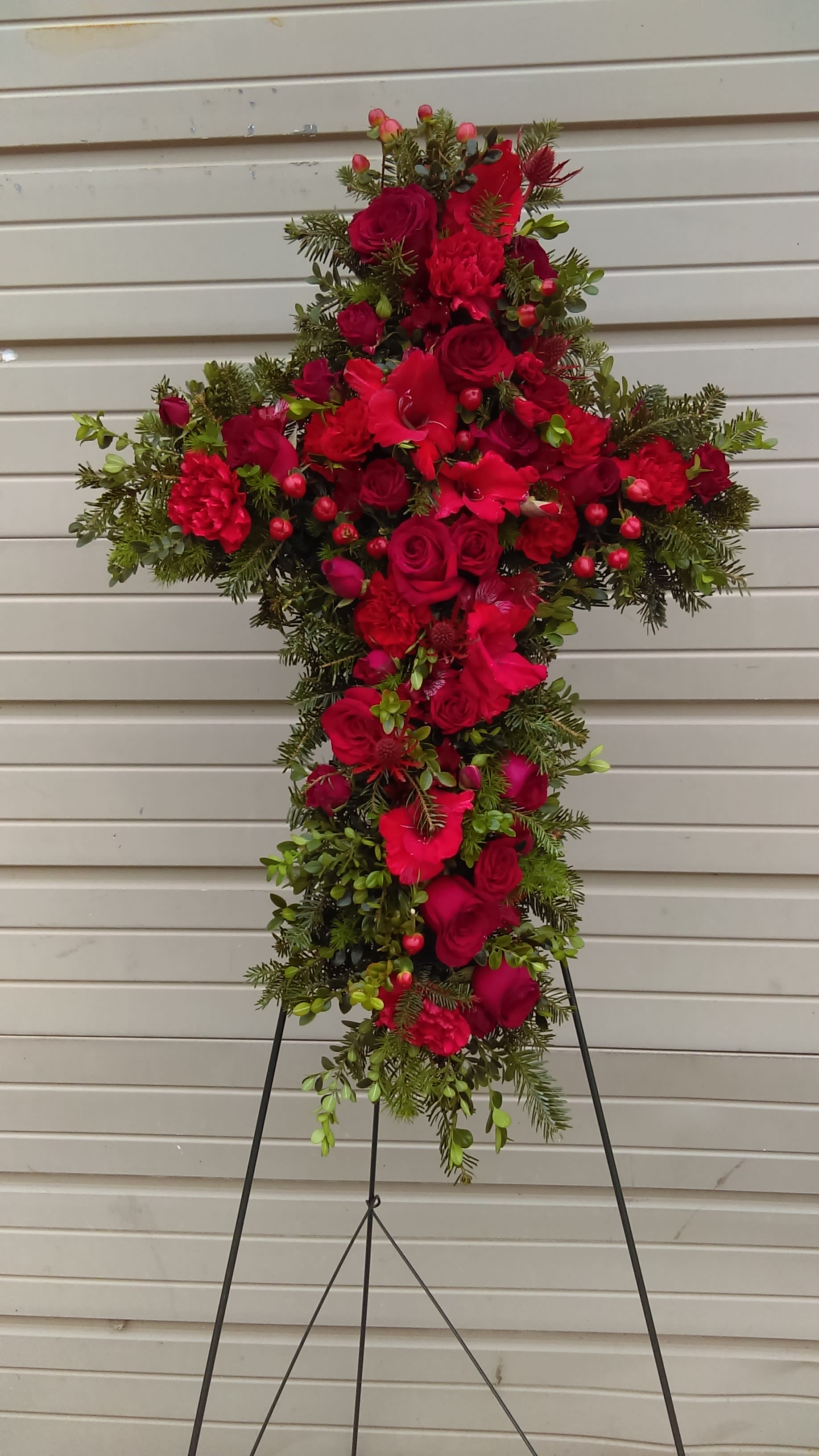 Cross Standing Spray - Shown here with red roses, red gladiolas and red hypericum berries with greenery to accent, this standing cross spray can be made by our designers with flowers in the color of your choice or as pictured here. 