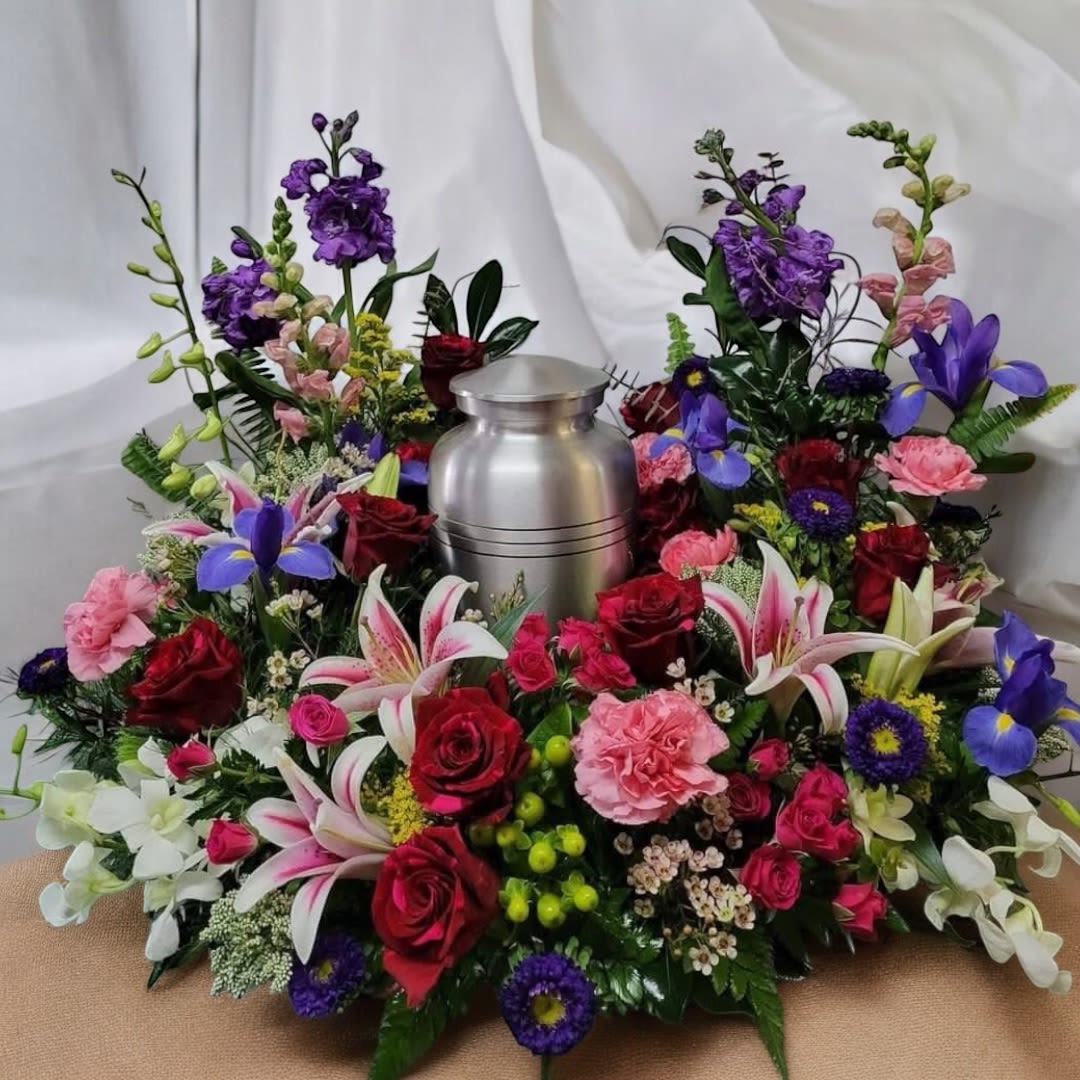 Peaceful Tribute - A stunning urn tribute designed with rich, heartfelt colors—featuring a silver urn surrounded by red and hot pink roses, pink lilies, purple irises, pink carnations, white orchids, and delicate filler blooms, finished with lush greenery. A full and elegant arrangement that expresses love, honor, and a beautiful farewell for a cherished soul.