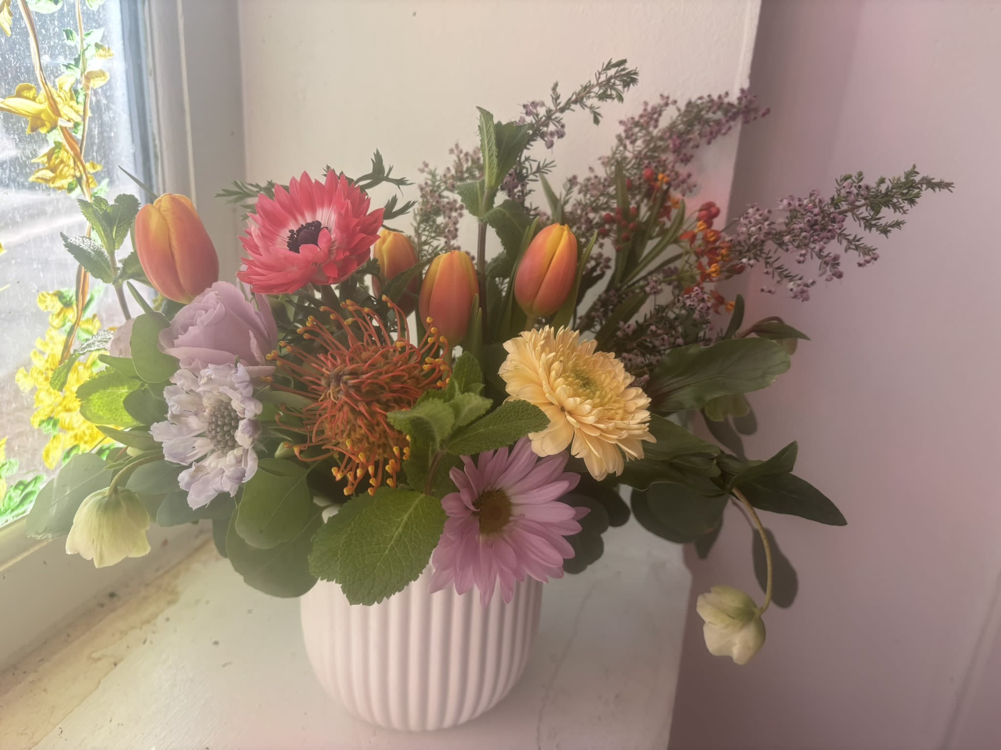 Enchanted - An arrangement that is filled with delight, colorful local tulips and anemones, scented local eucalyptus, Gerber daisies and flowering yellow acacia create a rose free arrangement that is filled with unique textures and colors.    Colors will vary as this arrangement is created based off what is available locally.    