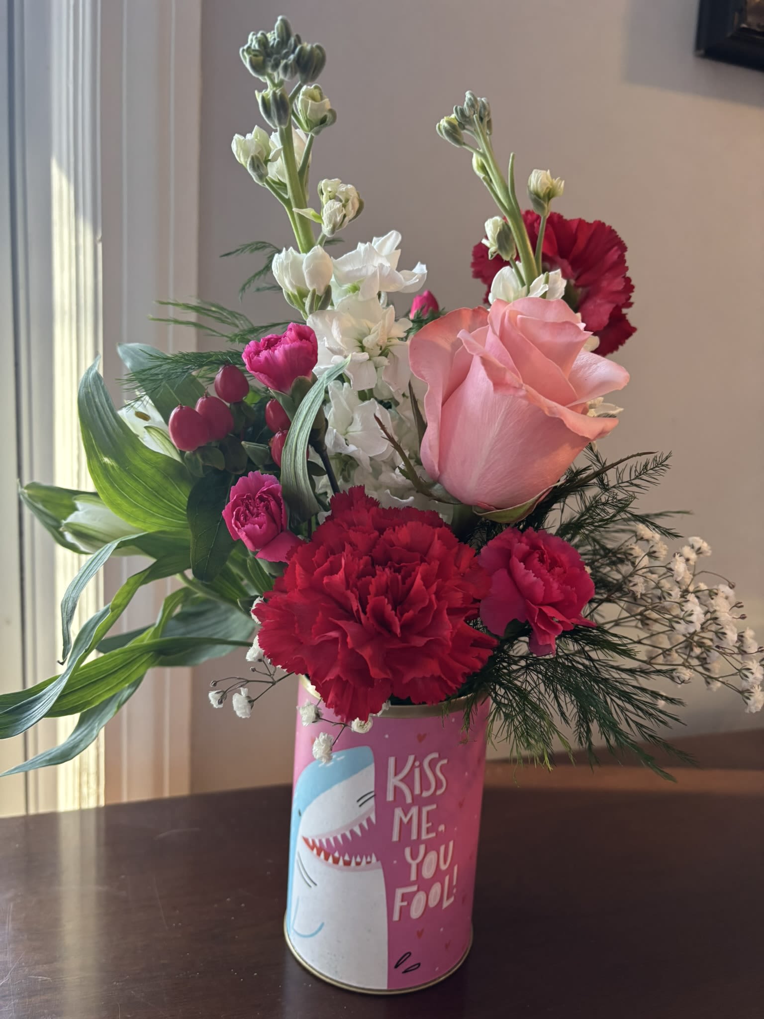 Lovin' Laughter - A colorful Valentine arrangement in a vessel that sends a message.  The flowers will be similar to the pictures, although the exact colors may vary.    In the notes when ordering please list your first and second choice of container saying.   1.  Kiss Me You Fool 2. The Perfect Match 3. Plant One on Me 4. Our Love is Fierce 