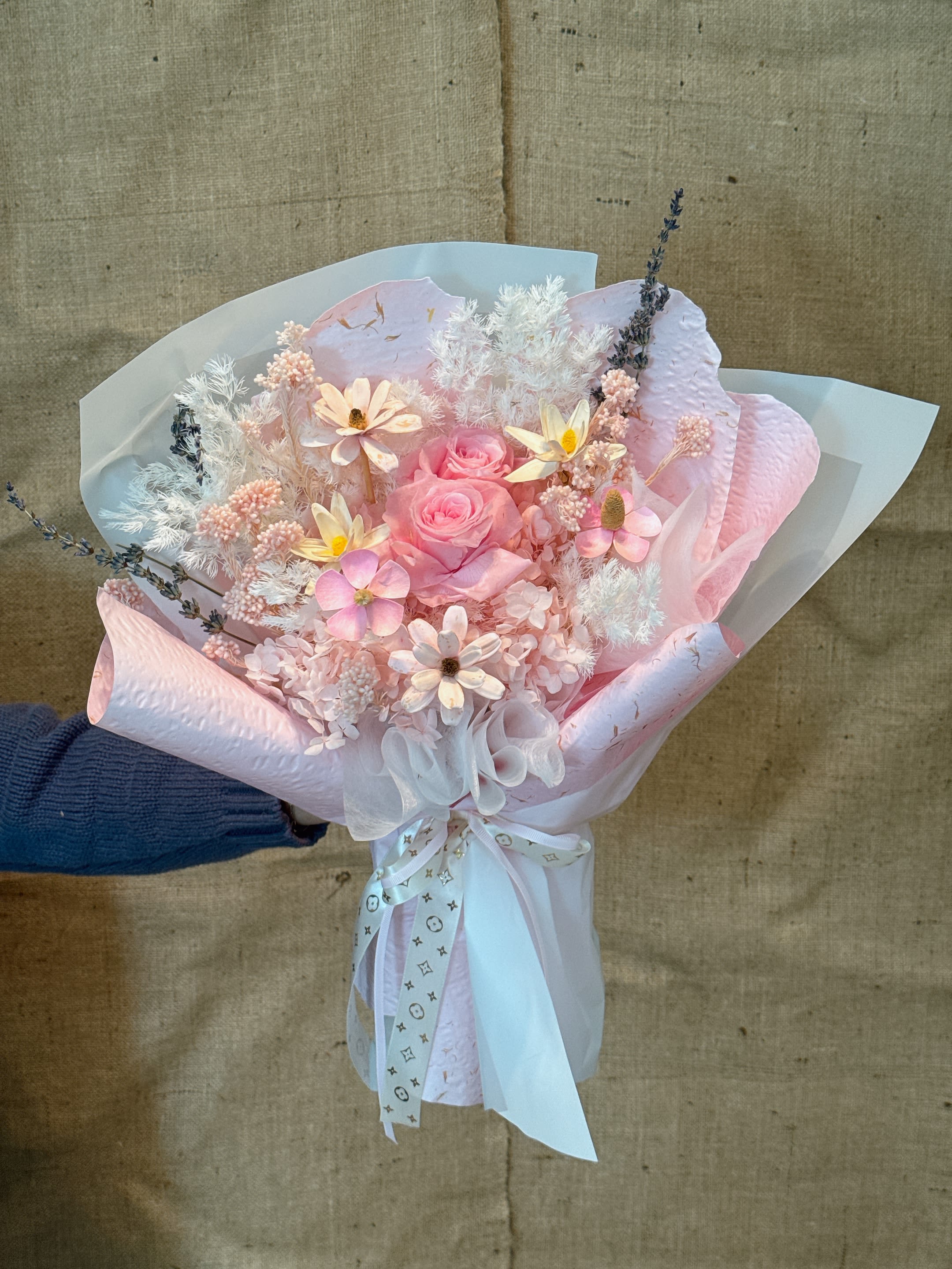 Soft as You - This is an immortal flower/dried flower bouquet with a soft pink tone. It mixes different forms of flowers, mainly including pink roses (eternal roses) and white, beige or light yellow fluffy flowers (such as full stars, hydrangeas or feather grass). Main characteristics: Color: The overall appearance is soft and romantic pink and white, and the color matching is warm and elegant. Flower type: It combines immortal flowers (real flowers are treated with special technology) and natural dried flower materials. Packaging: The bouquet is made of transparent and light pink wrapping paper, with light ribbon bows, Korean style and exquisite. Meaning: Pink immortal flowers usually symbolize eternal love, romance and delicate feelings. Due to its durability, it also represents an eternal commitment or friendship.