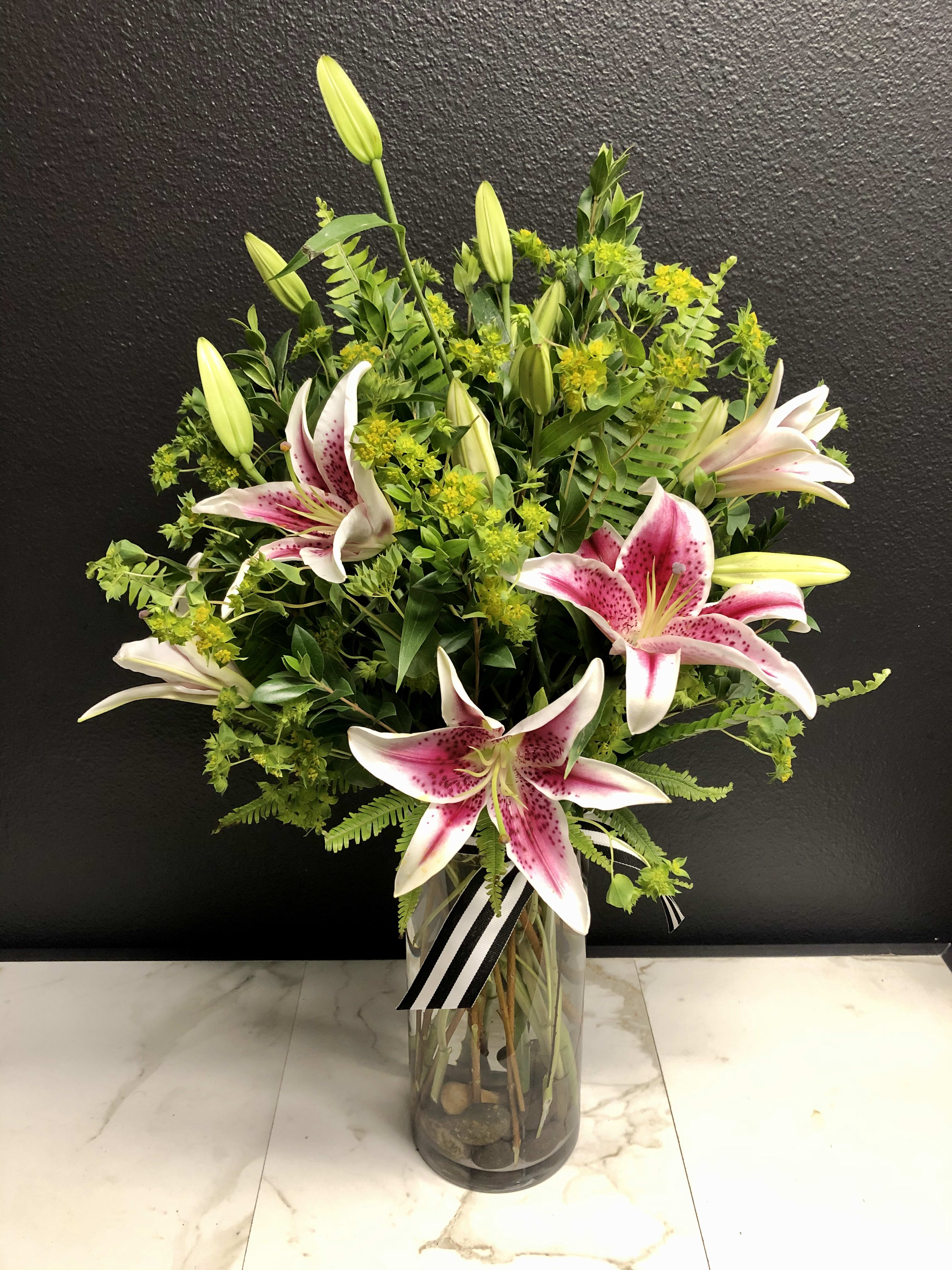 Pink Lilies En Masse  - A fragrant arrangement of our most beautiful Pink Oriental Lilies accented with seasonal greenery. Arranged upright, in a clear glass vase.  Overall design is approximately 24" x 15" The scale and stem count of this arrangement will increase in the Deluxe &amp; Premium price points.   