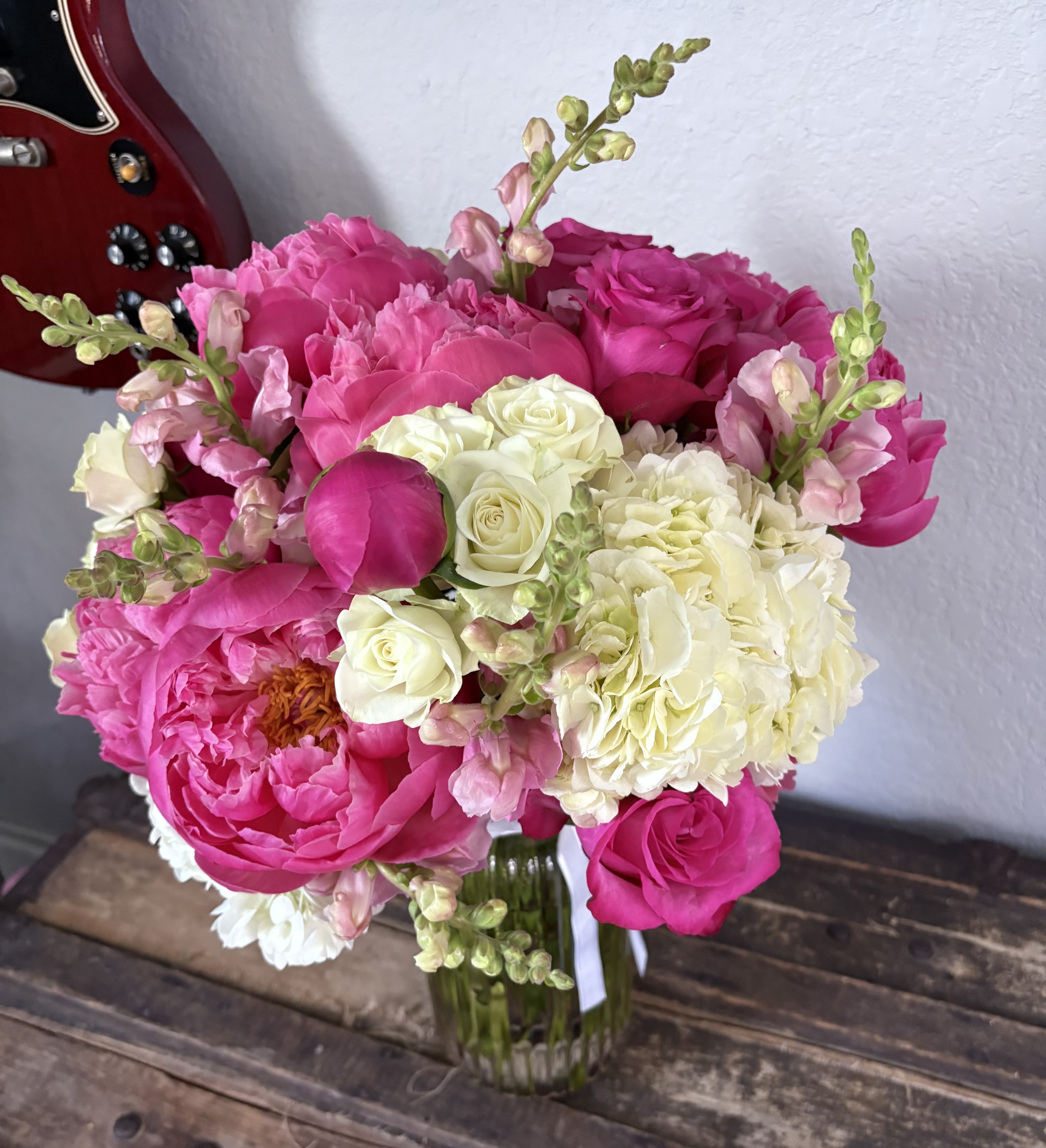 Queen's Elegance - An exquisite bouquet celebrating regal beauty, featuring majestic pink peonies surrounded by delicate white roses and graceful pink snapdragons. Arranged in a ribbed glass vase, this lush and vibrant display exudes the elegance befitting a queen, bringing a touch of royalty to any setting. Standard size includes :  10 pink peonies   Deluxe size: 12 pink peonies   Premium size:  15 pink peonies 