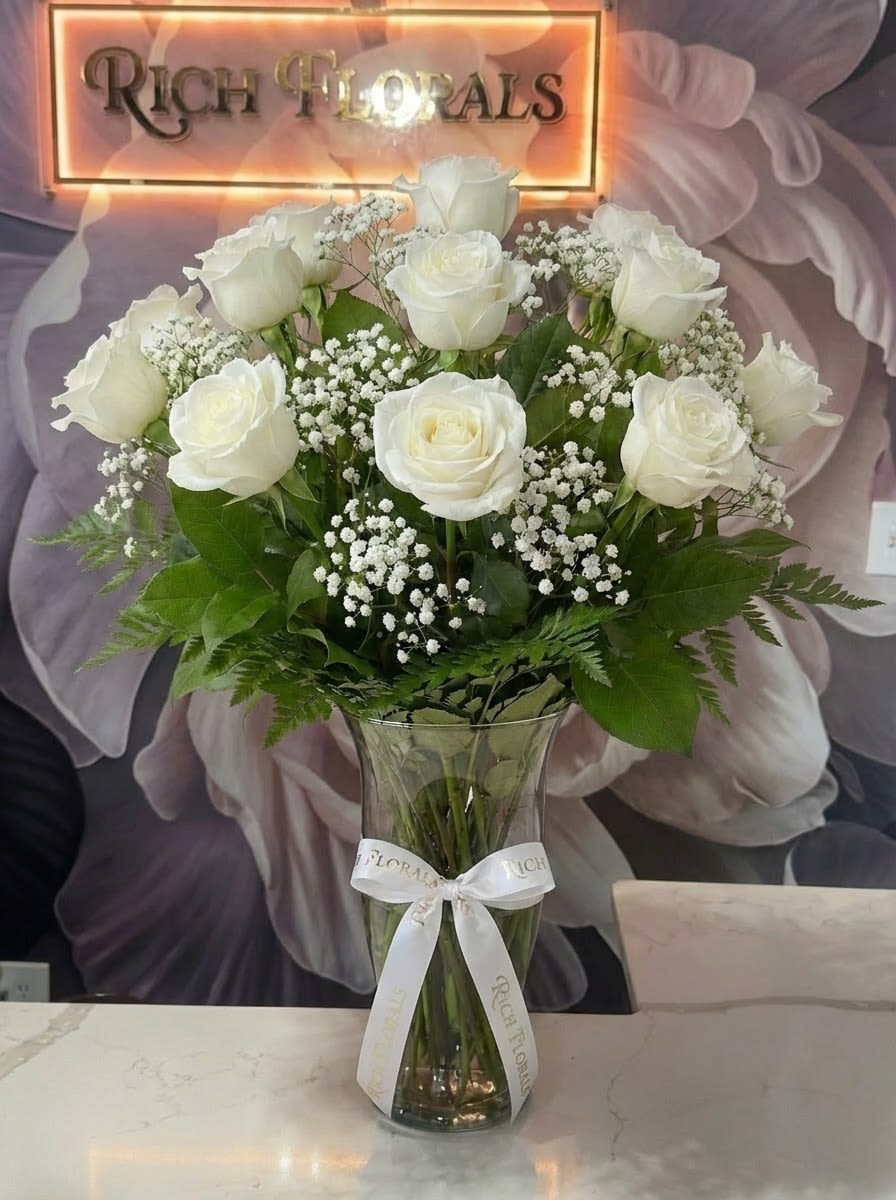 Long Stemmed White Roses - A serene arrangement where the timeless elegance of a dozen long stem white roses beautifully intertwines with the soothing lush greenery.  Each bloom in this white rose ensemble is carefully selected to symbolize purity, tranquility, and heartfelt sentiments.