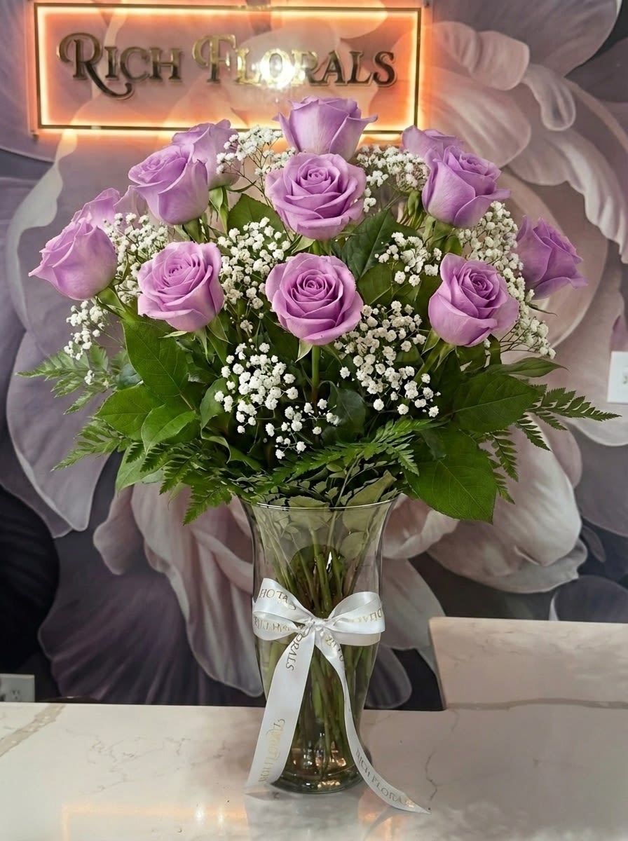 Dozen Long Stem Lavender Roses - Immerse yourself in the enchanting allure of our Dozen Long Stem Lavender Roses with assorted greenery, all elegantly presented in a classic vase. Each rose stands tall, radiating grace and elegance with its captivating lavender hue.   Standard - 1 dozen roses Deluxe - 2 dozen roses Premium - 3 dozen roses