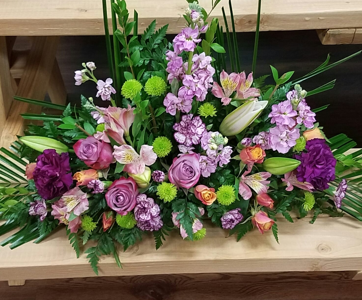 Purple Beloved One Sided Centerpiece - Purple Carnations and lillies, purple stock and purple roses.  This is a one sided centerpiece with green buttons and gold ruscus fillers its about 15 inches wide