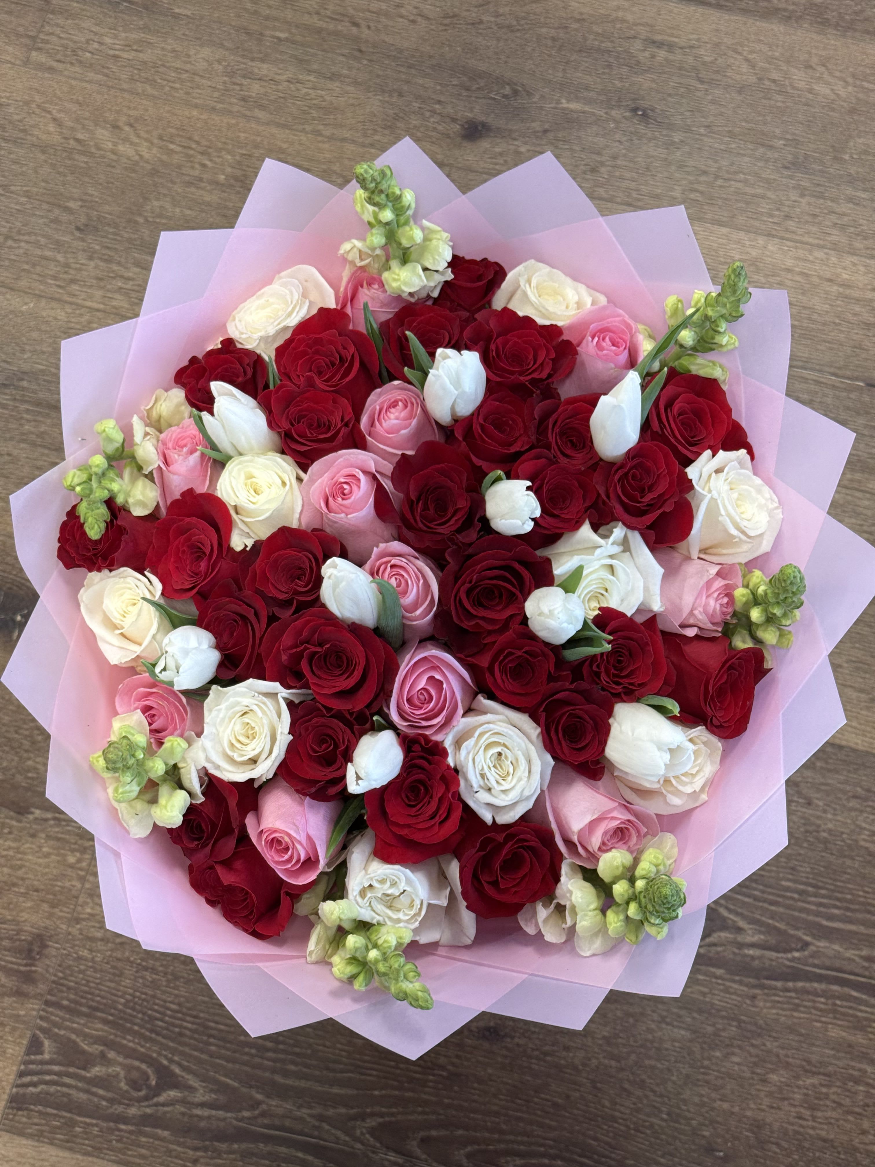 Sweet Symphony Bouquet  - This arrangement includes a a mixture of red, pink, and white long stem roses. Incorporated into the bouquet are white tulips and snapdragon wrapped in pink Korean waterproof paper.  *Pictured is the deluxe with 50 roses*