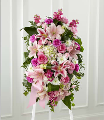 Gently into the Ever After - Bright, fresh, beautiful and just right for an elegant expression of heartfelt sorrow and devastating loss. This classic standing arrangement is constructed by a local FTD artisan florist of hand-selected pink blossoms ranging from pale pastels to deep blushing pink. It includes roses, carnations, stock, cushion pompons, Asiatic and Stargazer lilies and hydrangea beautifully set among a field of lush contrasting greens like aspidistra and ivy vines. It comes with a wooden easel for flexible display options and makes an impressive memorable tribute at a wake, funeral or graveside service. 