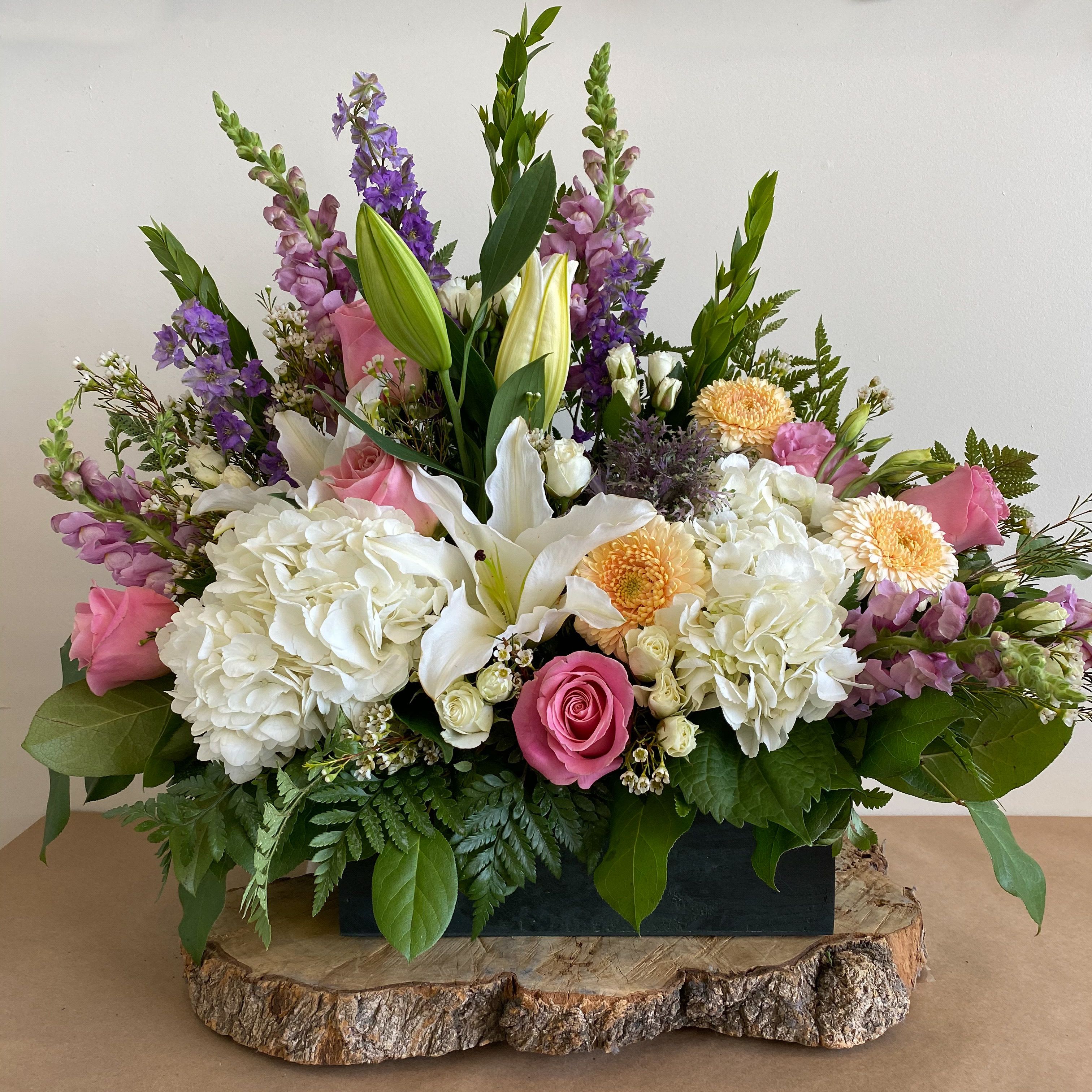 colorful box - Product Information Theme Colors: Shades of white, pink, purple, Peach, and green  Arranged in a wooden box  Featured Blooms: Roses, Hydrangeas, Lilies, Snapdragon, Delphiniums, Chrysanthemums, and greens  HK Flowers have a uniqueness of florals and seasonal blooms, certain flowers or colors may not be available as each season affects the availability, color, size, and shape of each floral bloom. Some flowers may be substituted accordingly.  Photos are used as a reference for the color palette and is NOT indicated of the final product. We ask for your trust in us that we will pick out the best seasonal available blooms, while still capturing the arrangements' theme and colors mentioned above.