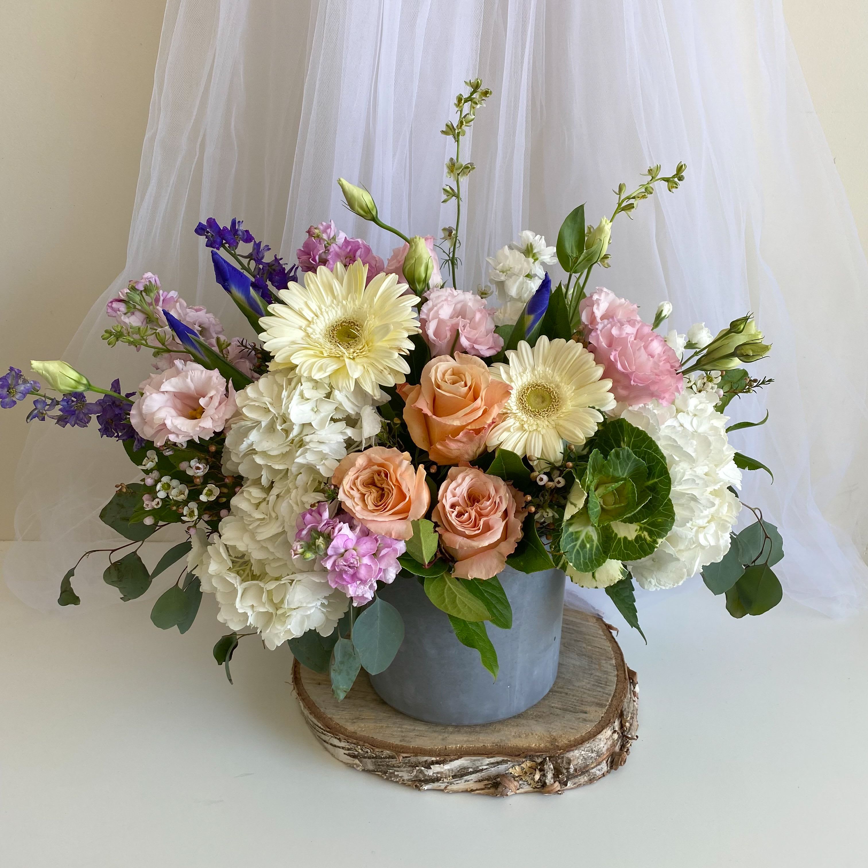 Lush Bloom - Theme Colors: Shades of whites with hints of purple  Featured Blooms: Daisies, Hydrangea, Roses, Gerbera, Delphinium, Lisia thus,  Seasonal Blooms.  HK Flowers have a uniqueness of florals and seasonal blooms, certain flowers or colors may not be available as each season affects the availability, color, size, and shape of each floral bloom. Some flowers may be substituted accordingly.  Photos are used as a reference for the color palette and is NOT indicated of the final product. We ask for your trust in us that we will pick out the best seasonal available blooms, while still capturing the arrangements theme and colors mentioned above.