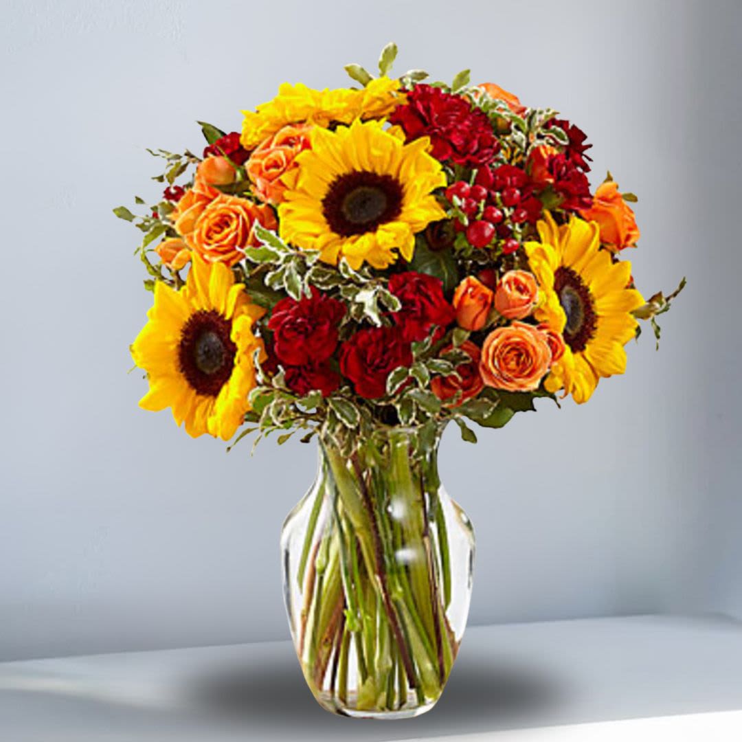 An Autumn Frenzy - Bouquet is set to create harvest happiness wherever it may be sent! Bold and beautiful, this bouquet showcases an array of fall color, bringing together eye-catching mini sunflowers, burgundy mini carnations, orange spray roses, and red hypericum berries, accented with lush greens. Presented in a clear glass vase, this stunning fall flower arrangement is set to send your warmest wishes of love and gratitude to your favorite friends and family in honor of Thanksgiving, as a way to express your thanks and gratitude, or in celebration of a fall birthday. 