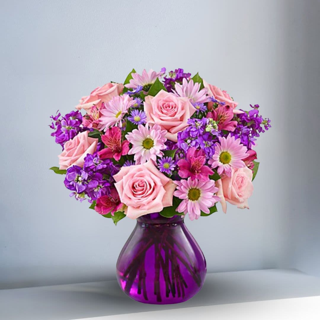 Lavender Dreams - Send her this truly original bouquet of lovely roses, daisy poms, stock, alstroemeria and monte casino in shades of pink and purple. Delivered in a stylish purple glass vase to bring out the richness of color -- and help you express yourself perfectly. Hand-crafted arrangement of roses, daisy poms, alstroemeria, stock, monte casino and salal created in honor of Womenâs Week Artistically designed by our expert florists in a chic purple glass vase.