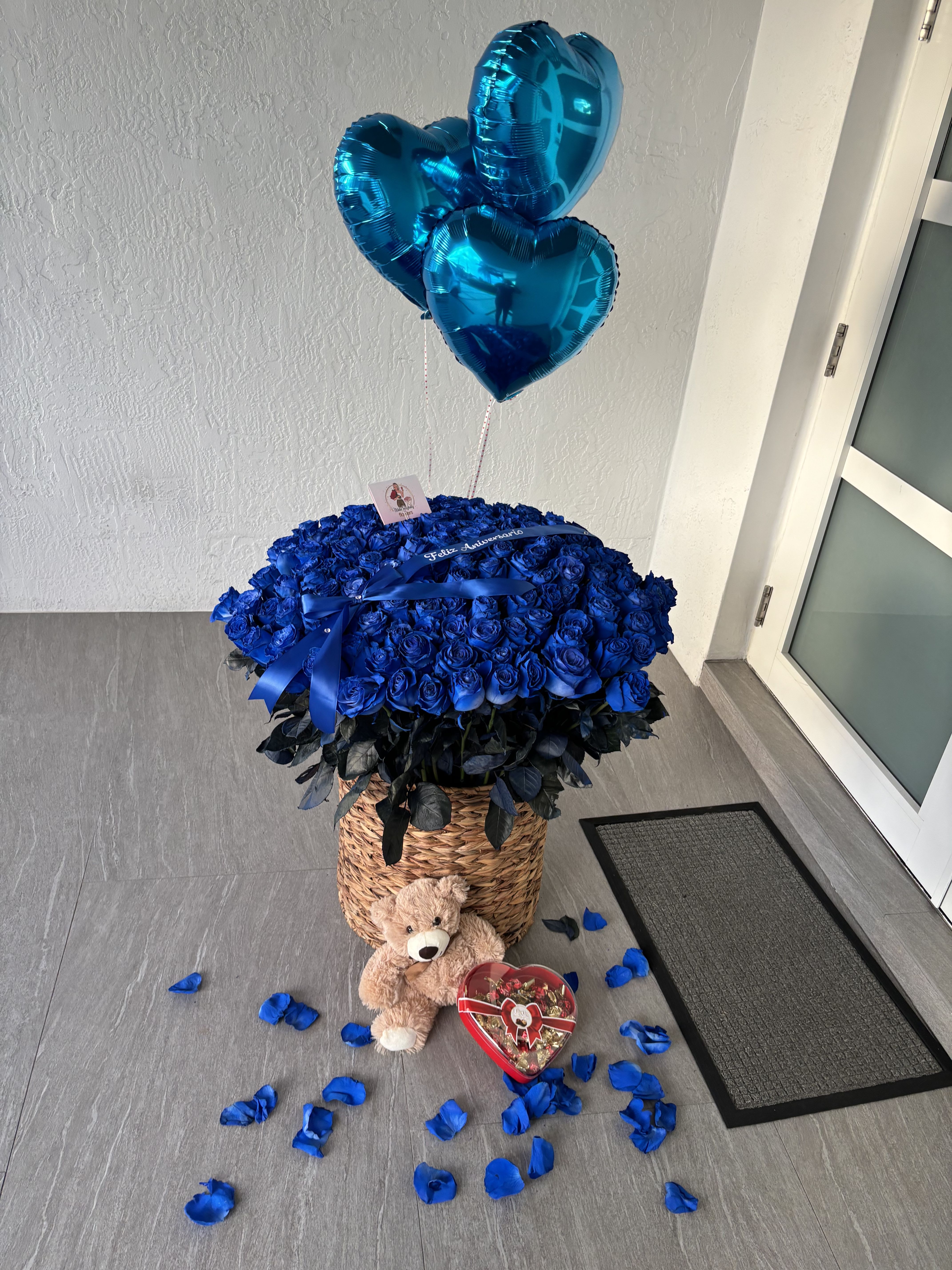 Luxury Blue Roses Arrangement with Teddy &amp; Chocolates - Luxury Blue Roses Arrangement with Teddy &amp; Chocolates Surprise your loved one with this stunning gift set featuring an elegant basket overflowing with vibrant blue roses, beautifully accented with satin ribbons. Accompanied by a cuddly teddy bear, heart-shaped chocolates, and metallic blue heart balloons, this arrangement is the perfect expression of love, celebration, or appreciation. Petals scattered around add an extra touch of romance, making it an unforgettable gesture for any special occasion.