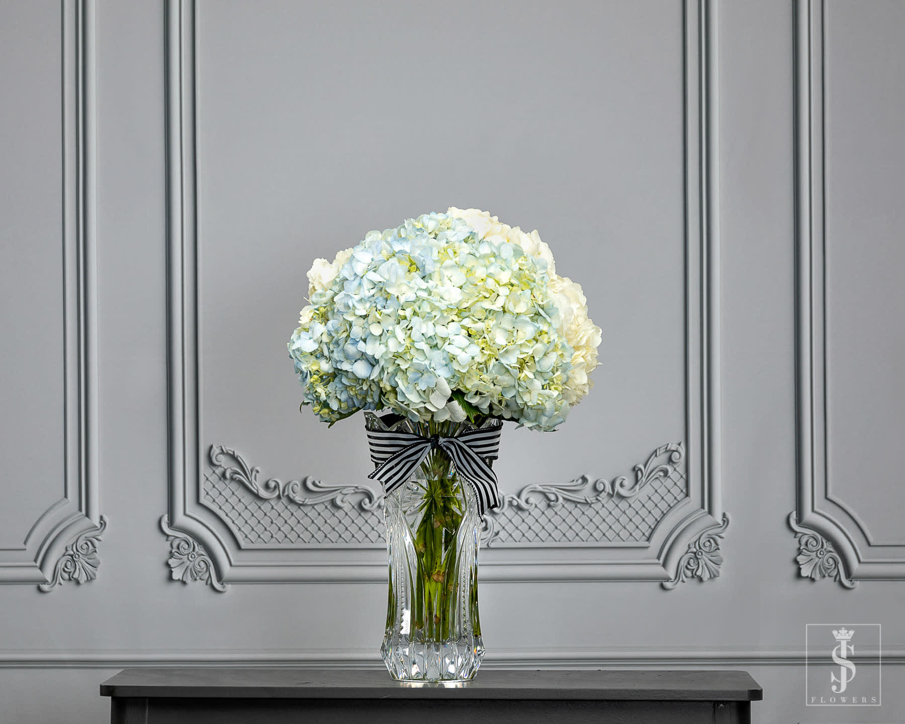 Blue Hydrangeas - This item is sold by the stem in multiples of 8. Stems/Bunch: 8 stems per wrap.  Bring a lush, textured feel to your arrangements or bouquets with these utterly exquisite large blue hydrangeas from JS Flowers. Especially ideal for baby showers, bridal showers, and beach-themed weddings, these big and bold beauties offer a creamy, watercolor-like texture. The large 4- to 6-inch wide blooms can easily be used as the central flower of your centerpieces to add extra volume and work well with any blue, green or white color scheme.  The hydrangea has long been a wedding and special event favorite, and only gets more popular. Said to symbolize deep emotion and gratitude, the hydrangea is a lush, fluffy flower that’s a downright backyard garden classic. Hydrangeas also tend to be more affordable than other large-blossom flowers, so they’re a great choice for DIY brides on a budgering a lush, textured feel to your arrangements or bouquets with these utterly exquisite large blue hydrangeas from JS Flowers. Especially ideal for baby showers, bridal showers, and beach-themed weddings, these big and bold beauties offer a creamy, watercolor-like texture. The large 4- to 6-inch wide blooms can easily be used as the central flower of your centerpieces to add extra volume and work well with any blue, green or white color scheme.  Call us for Wholesale Pricing (469)900-8095  Send your Beautifully Wrapped Fresh Flowers today. The stems will arrive wrapped in  JS Flowers tissue and cellophane.. **Please note the vase is not included!   Important Information:  * Orders placed on Monday will process on Tuesday for Wednesday delivery.  * Orders placed on Tuesday will process on Wednesday for Thursday delivery.  * Orders placed on Wednesday will process on Thursday for Friday delivery.  * Orders placed from Thursday to Sunday will process on the following Monday for Tuesday delivery.  * Orders will not be delivered on Saturdays and Sundays.   All flowers are Shipped/Delivered during their freshest state so that you can enjoy them for as long as possible! Please be aware that upon arrival flower heads will be tight, allowing you to enjoy every moment of them maturing into full blooms! Photos displayed on this website are taken during each flowers most mature state.  