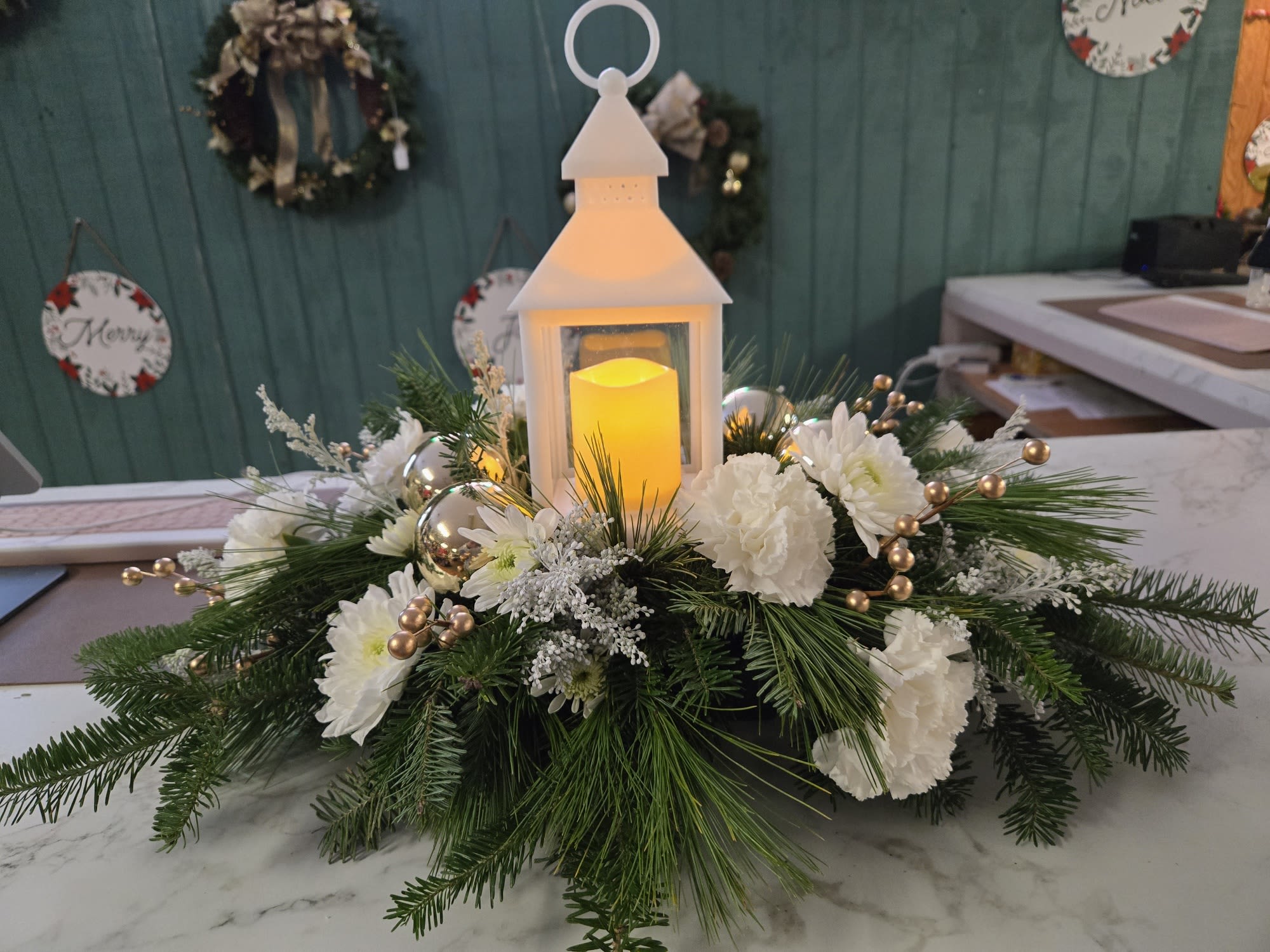 Light The Night -  Light the Night arrangement, featuring a beautifully crafted working white lantern keepsake at its heart. This is versatile arrangement that can be used for many occasions.  For Memorials, For Holidays. The soft glow of the lantern brings warmth, and charm to any space.  The lantern sits in the middle of greens and flowers- appropriate to the season or occasion  Elegant yet inviting, Light the Night adds a gentle sparkle to an occasion—creating a peaceful, glowing moment wherever it’s placed.