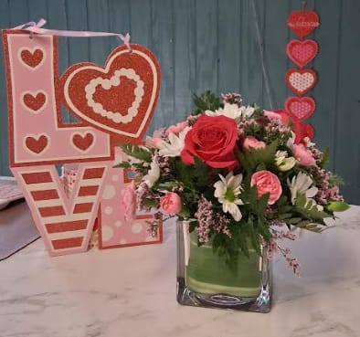 Sweet Talk - A charming arrangement designed to say it all. Sweet Talk features lush greens accented with elegant aspidistra ribbon, classic roses, cheerful mini carnations, bright daisies, and playful filler blooms. Fresh, fun, and full of personality—this arrangement is perfect for sending a little love, joy, or just-because happiness.