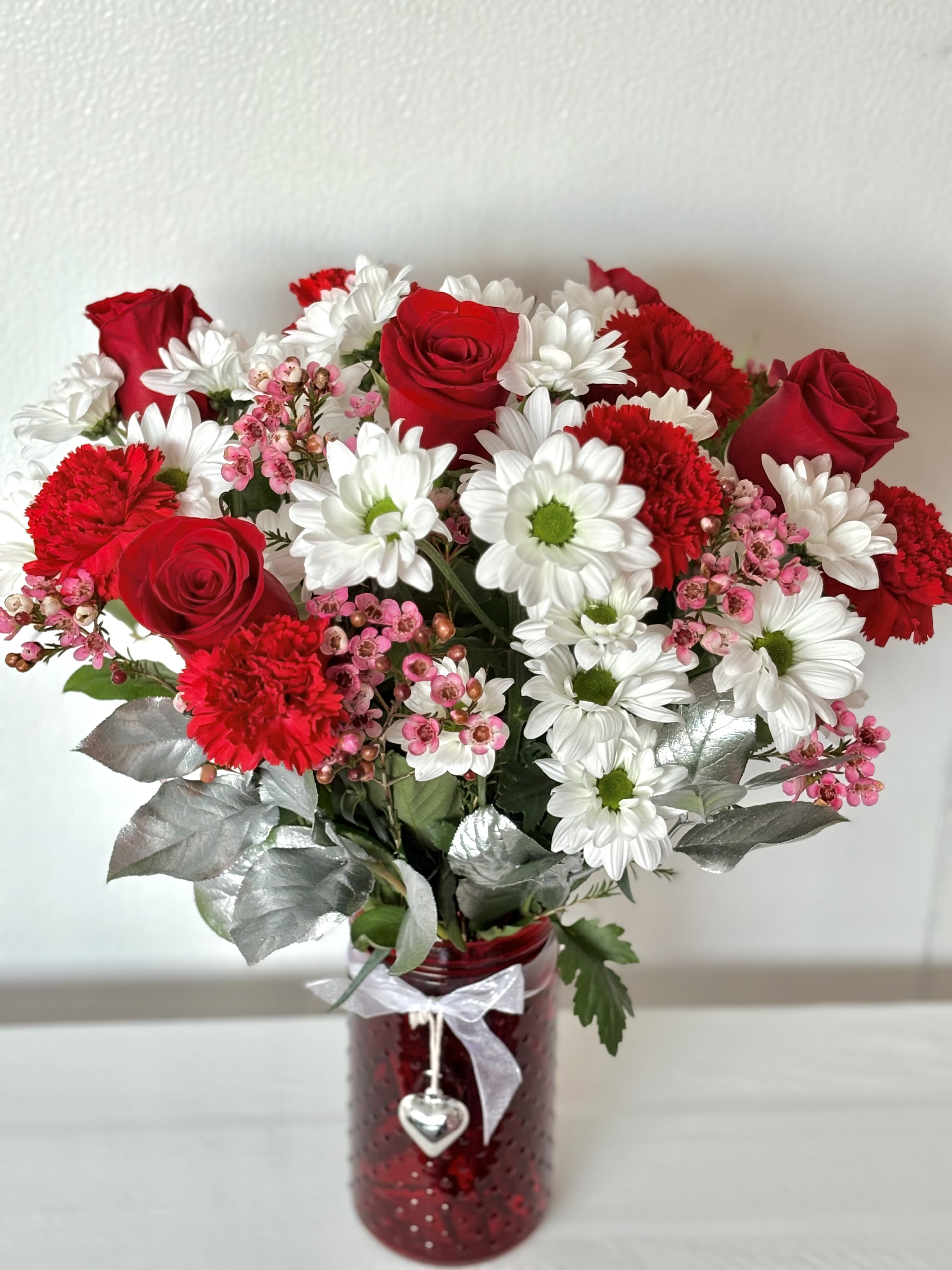 Love Jar - Daisies, red roses, red carnations, and wax flower make up this love jar. Arrangement measures approximately 20-22 inches. 