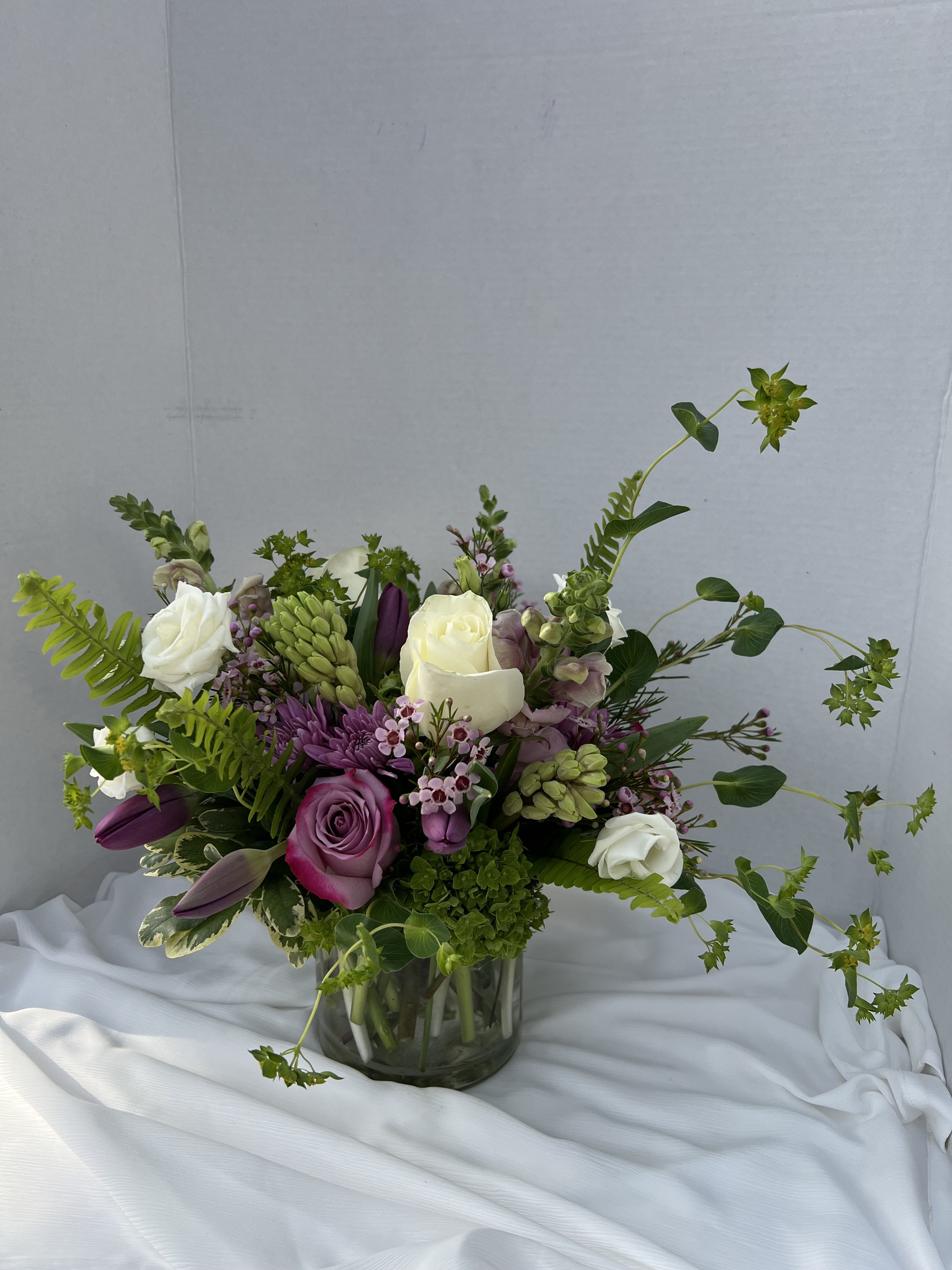 Lavender Love - Lavender Love is a soft, garden-inspired arrangement that feels effortlessly romantic. Hyacinths nestle among lush green hydrangeas, their gentle textures creating a full, cloud-like base. Graceful purple tulips rise through the design, adding movement. Airy garden greens weave throughout, dotted with whispers of lavender that bring a calming, dreamy finish.  