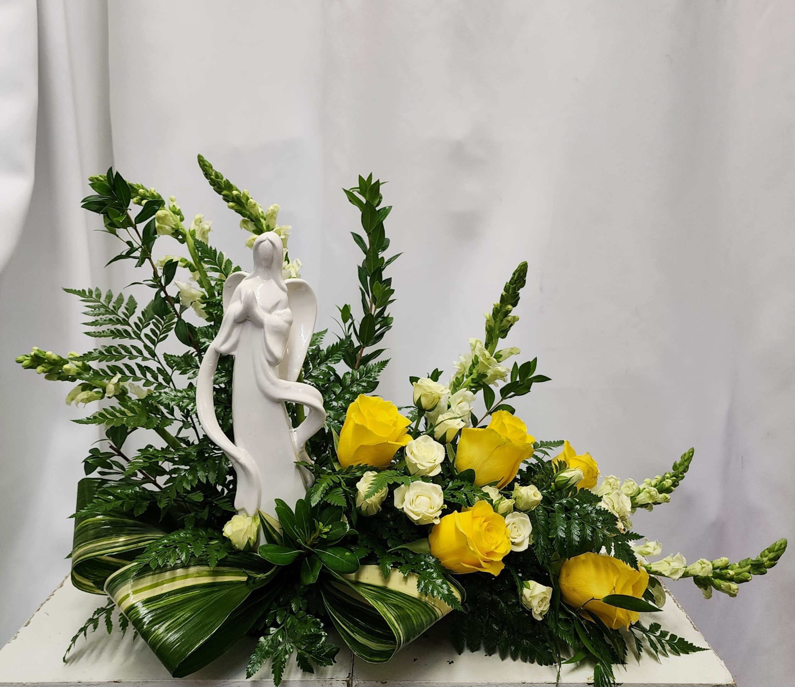 Modern Angel Tribute Keepsake in Yellow - TPP - A keepsake memorial Angel is placed in a garden of beautiful blooms. Shown in shades of yellow and white, this arrangement can be done in many colors. For specific colors and please list your preference in the notes section of the order. 