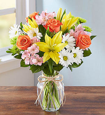 Fields of Europe - The rustic beauty of hand tied bouquets fresh from a European flower market come alive in our best-selling arrangement. Handcrafted by our skilled artisan florists, this vibrant mix is gathered inside a clear glass vase tied with raffia for a touch of Old World charm.  All-around arrangement with orange roses; yellow Asiatic lilies; pink alstroemeria) athos pom; white daisy poms; accented with salal tips (z) Artistically designed in a 8" clear glass vase tied with raffia Regular arrangement measures approximately 15"H x 12"W Deluxe arrangement measures approximately 17"H x 14"W Premium arrangement measures approximately 18"H x 14"W