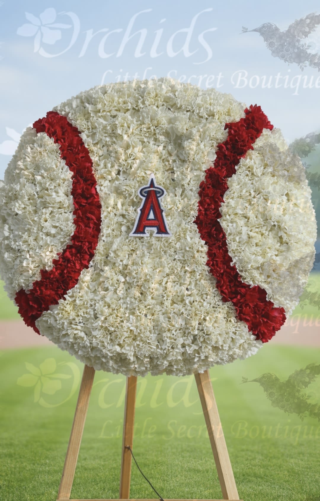 The OLSB Baseball  Funeral Standing  Spray  - Offer a meaningful expression of sympathy and love with this unique, custom-designed baseball standing spray. Featuring the Angels patch logo and made with fresh white and red carnations to form the shape of a baseball. The baseball wreath base is 18" x 18" inches and will be placed in a 5 1/2" easel wood stand. Perfect for any Angels baseball fan! It's a wonderful way to remember the deceased and their favorite pastime at their memorial service.