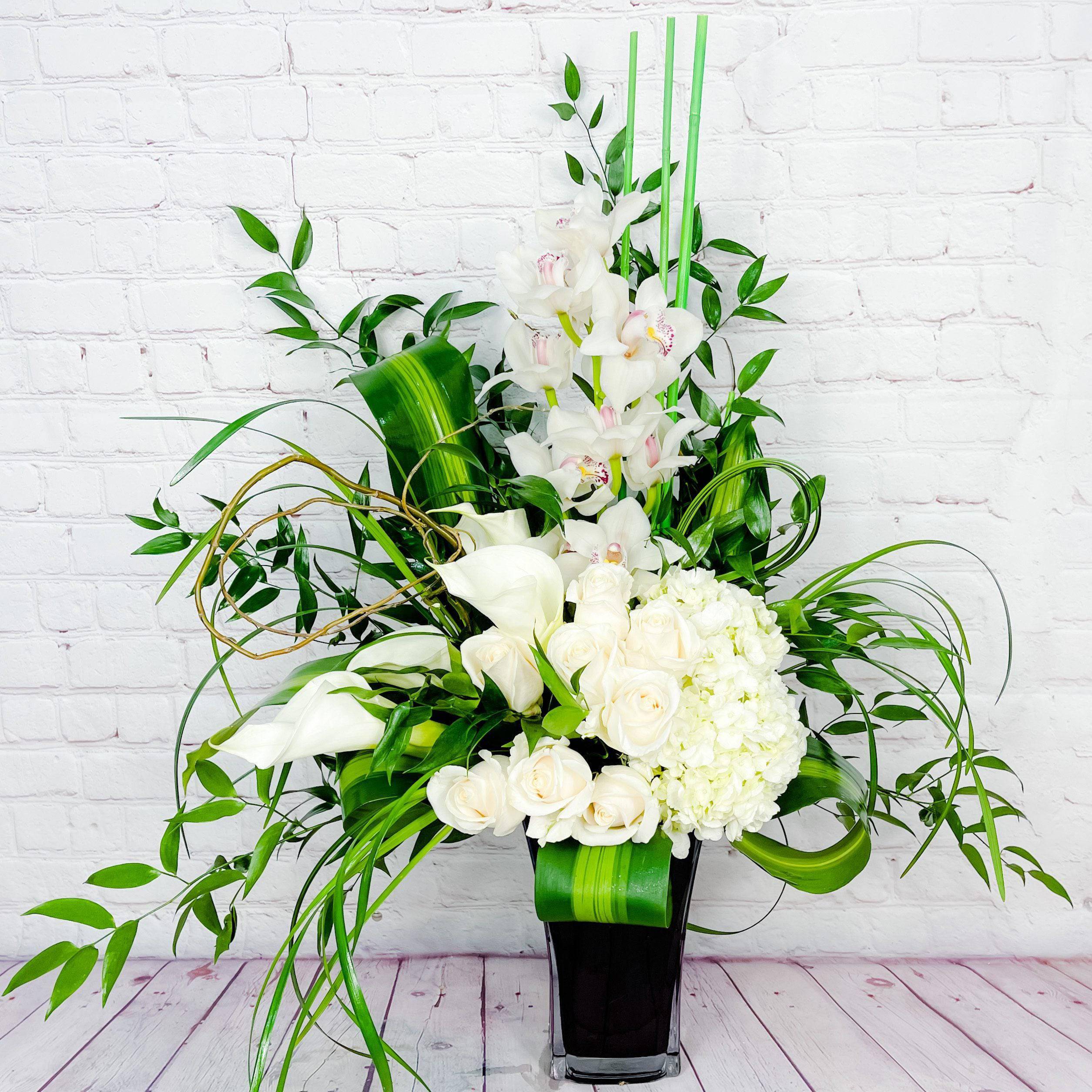 White Sophistication by DGM Flowers - Our gorgeous White Sophistication arrangement is made of an assortment of sophisticated white flowers including cymbidium orchids, mini calla lilies, roses, and hydrangea complimented by a tall glass vase.   --   Our gorgeous White Sophistication arrangement is made of an assortment of sophisticated white flowers including cymbidium orchids, mini calla lilies, roses, and hydrangea complimented by a tall glass vase.  Approximately 32"H X 28"W