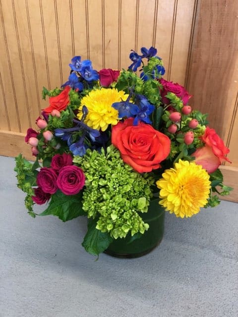 Color Joy - An explosion of colorful blooms. Green hydrangea, bright yellow and orange roses, blue delphinium, hypericum berries and more. Perfect for any occasion. Version shown is the deluxe.
