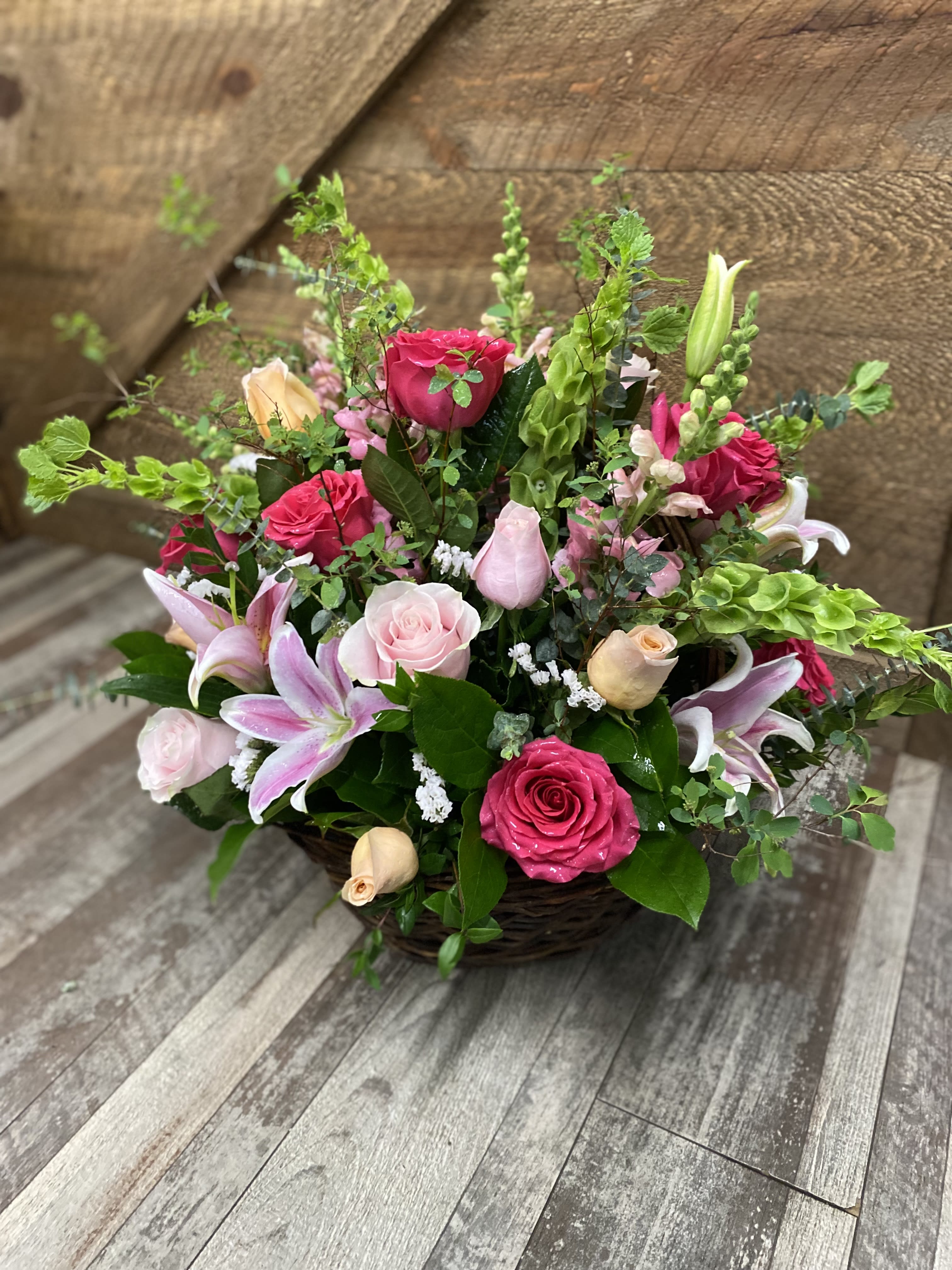 Harmony  - A beautiful basket arrangement designed garden style. Bells of Ireland, roses, lilies, snapdragons, statice and lush greenery. Version shown is the deluxe.