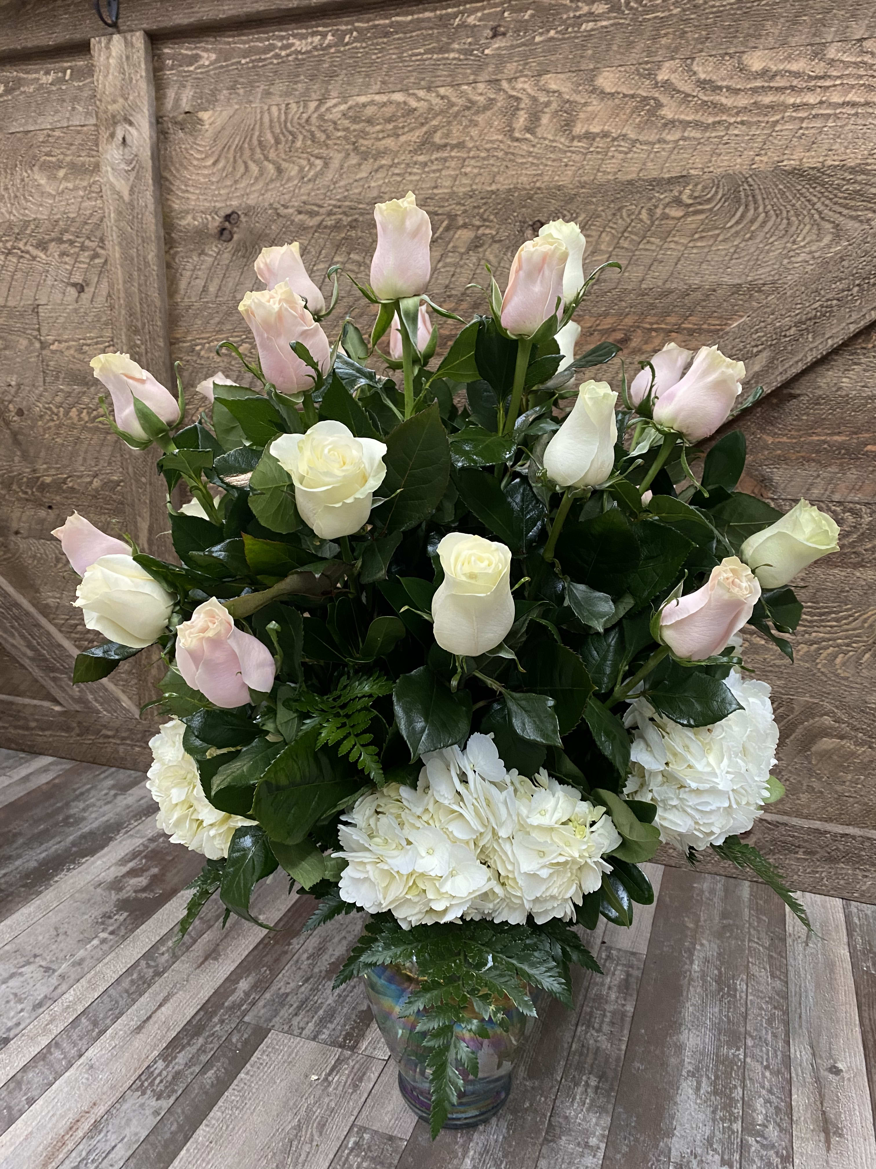 The Cathy - Pink and white roses arranged with hydrangeas and greenery.  Standard will include 1 dozen roses, deluxe 18 roses, and premium 2 dozen. Version shown is the deluxe.