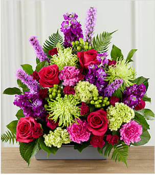  Warm Embrace™ Arrangement - A lovely way to say, "farewell," this bright, beautiful arrangement expresses your sympathy with color, texture and floral artistry, while comforting grieving friends and family. This handcrafted bouquet is handcrafted by a local FTD florist and makes a vibrant statement with hot pink roses, pink and fuchsia carnations, purple stock, green spider chrysanthemums, mini-hydrangea and hypericum berries all accented with sword fern and salal in a low rectangle container of silvery metallic plastic.  Your purchase includes a complimentary personalized gift message.