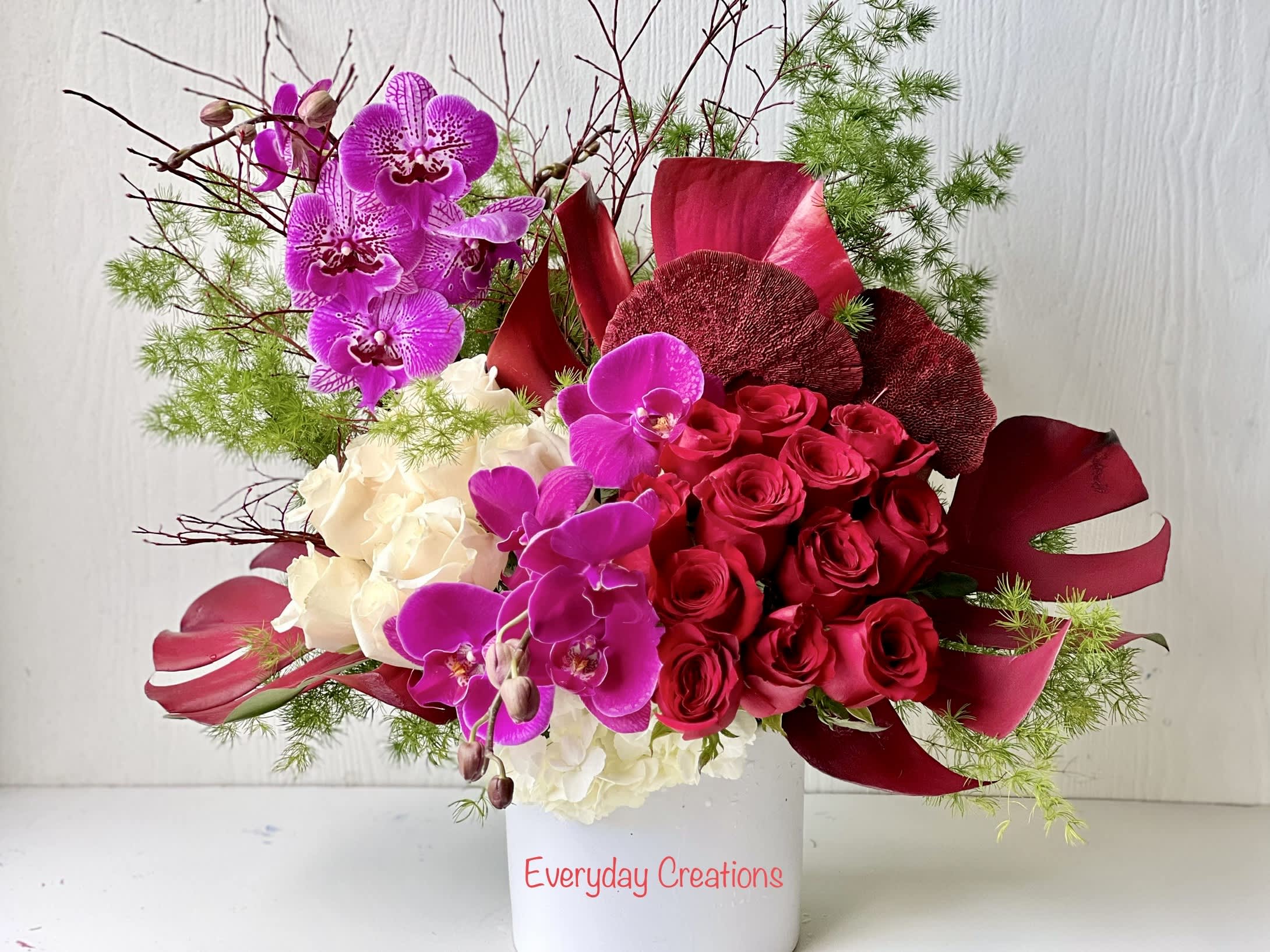 EC96 - Love Spell Bouquet - The Love Spell Bouquet is a luxurious and lavish floral arrangement that will surely capture anyone's attention. This arrangement is composed of roses, hydrangea, orchids and elegant and exotic tropical greenery all designed in a modern white ceramic cylinder. This statement piece is a perfect centerpiece for upscale events and romantic occasions and is a feast for the eyes! 