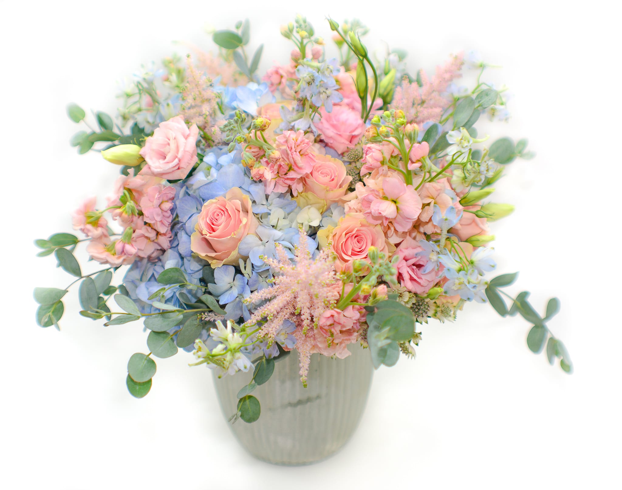 The Unicorn  - A stunning combination of colors, sweet and lovely. This jewel-toned bouquet includes some of our most loved flowers. Soft pink roses, peach matthiola, pink astilbe, baby blue hydrangea and blue delphinium.   A blue flower, it stands for desire, love, and the metaphysical striving for the infinite and unreachable. It symbolizes hope and the beauty of things. Comes in a glass white vase. 