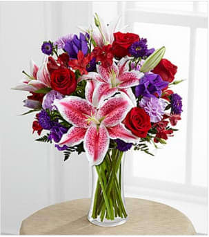 The Stunning Beauty™ Bouquet by FTD® -  Fragrant Stargazer lilies, red roses, lavender carnations, red Peruvian lilies, purple double lisianthus, and purple matsimoto asters and greens  in a classic CLEAR glass vase. 