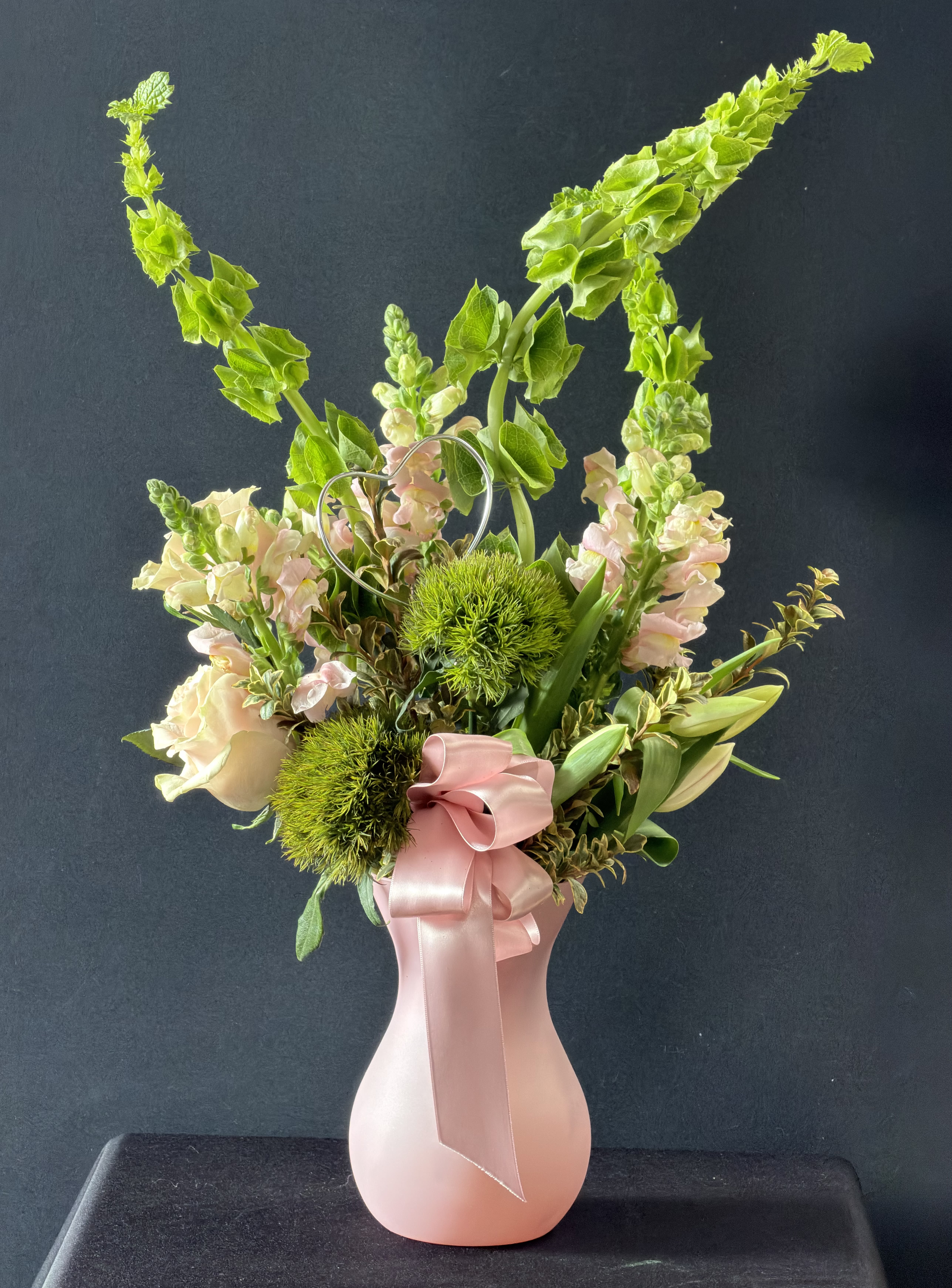 Pink Petals &amp; Serendipity Floral Arrangement - Charming and romantic, this pink floral arrangement showcases light pink roses, tulips, and snapdragons accented with Bells of Ireland and green trick, all artfully arranged in a Teleflora Pink Serendipity Vase.